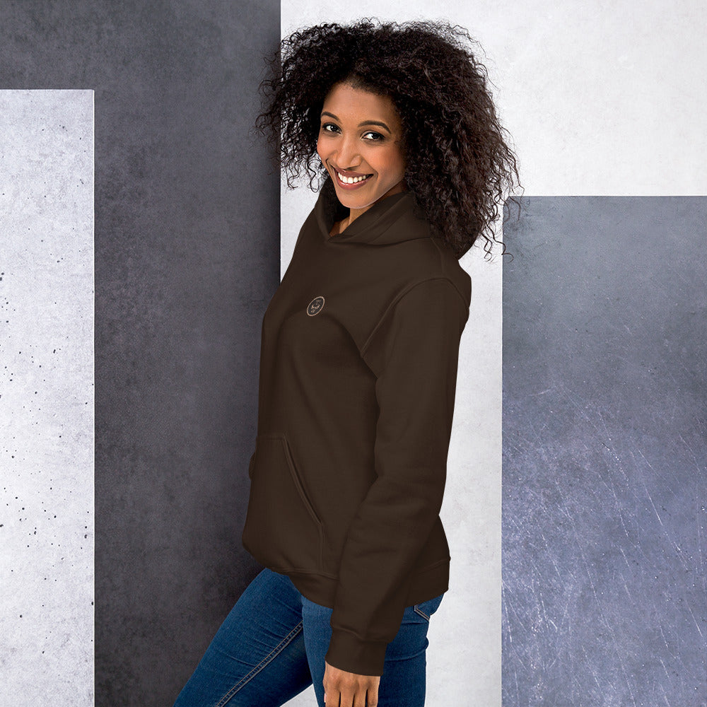 Ein weibliches Model zeigt sich lässig von der linken Seite tragend den Kapuzenpullover "The Chocolate One" mit Sicht auf das gestickte Eulen Emblem auf der linken Brusthöhe.