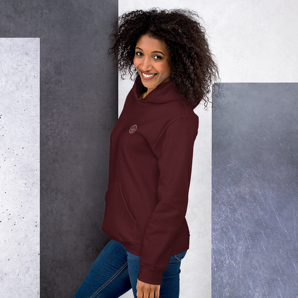 Ein weibliches Model zeigt sich lässig von der linken Seite tragend den Kapuzenpullover "The Maroon One" mit Sicht auf das gestickte Eulen Emblem auf der linken Brusthöhe.