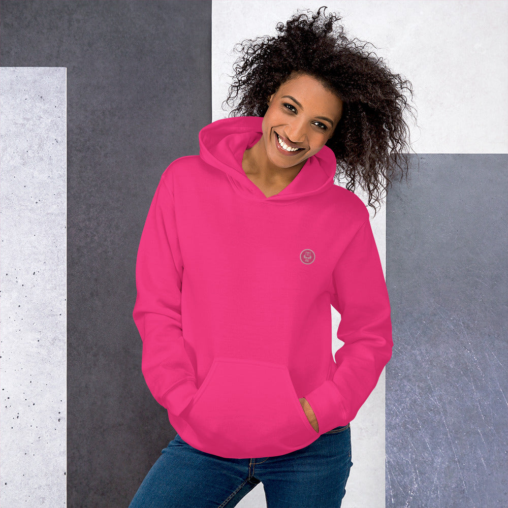 Ein weibliches Model zeigt sich mit dem Kapuzenpullover "The Pinky One" Beide Hände lässig in der vorderen Beuteltasche. 