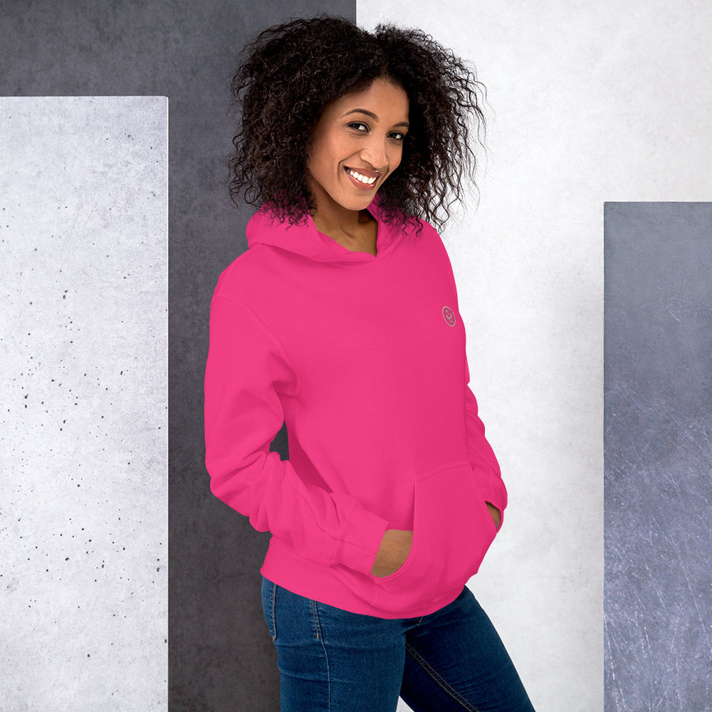 Ein weibliches Model lehnt lässig an einer Wand und zeigt tragend den "The Pinky One" Kapuzenpullover seitliche Vorderansicht mit beiden Händen in der vorderen Beuteltasche.