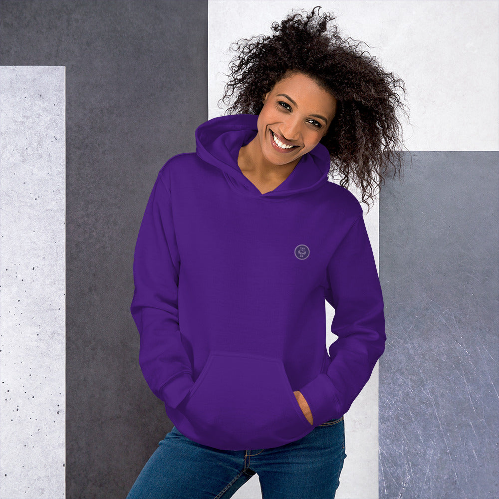 Ein weibliches Model zeigt sich mit dem Kapuzenpullover "The Purple One" Beide Hände lässig in der vorderen Beuteltasche.