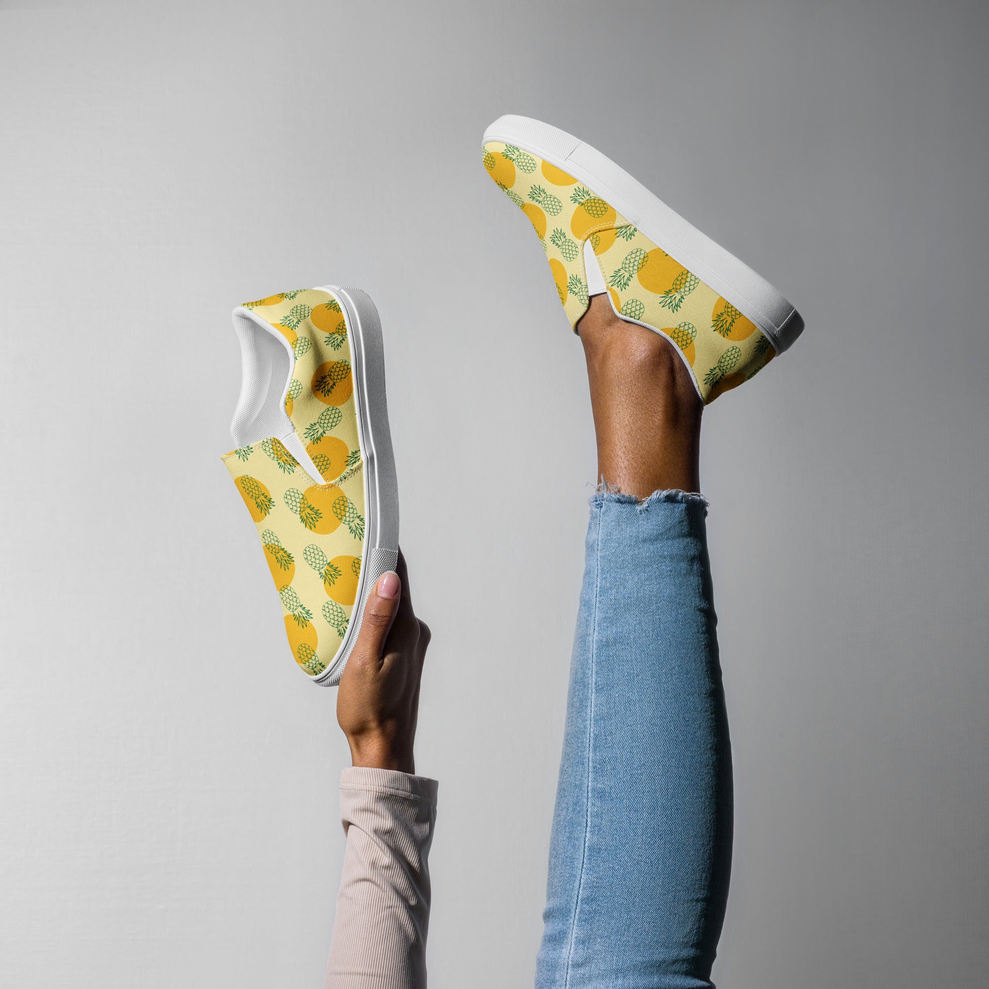Ein weibliches Model streckt ein Bein in die Luft und hält mit einer Hande den anderen Schuh mit einem Muster aus grünen Ananas-Outlines und orangen Kreisen auf gelben Hintergrund. Designed, by Just a Girl.
