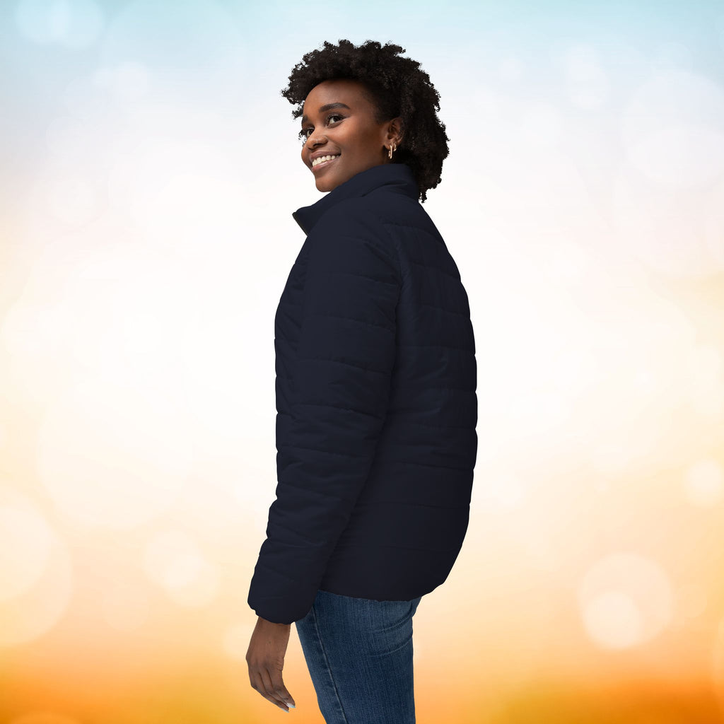 Das weibliche Model zeigt die linke Seite der Damen-Pufferjacke in einem Black Pearl Ton. Die Jacke ist horizontal gesteppt, hat eine glatte Oberfläche, einen hohen Stehkragen und einen durchgehenden Reißverschluss. Designed, by Just a Girl