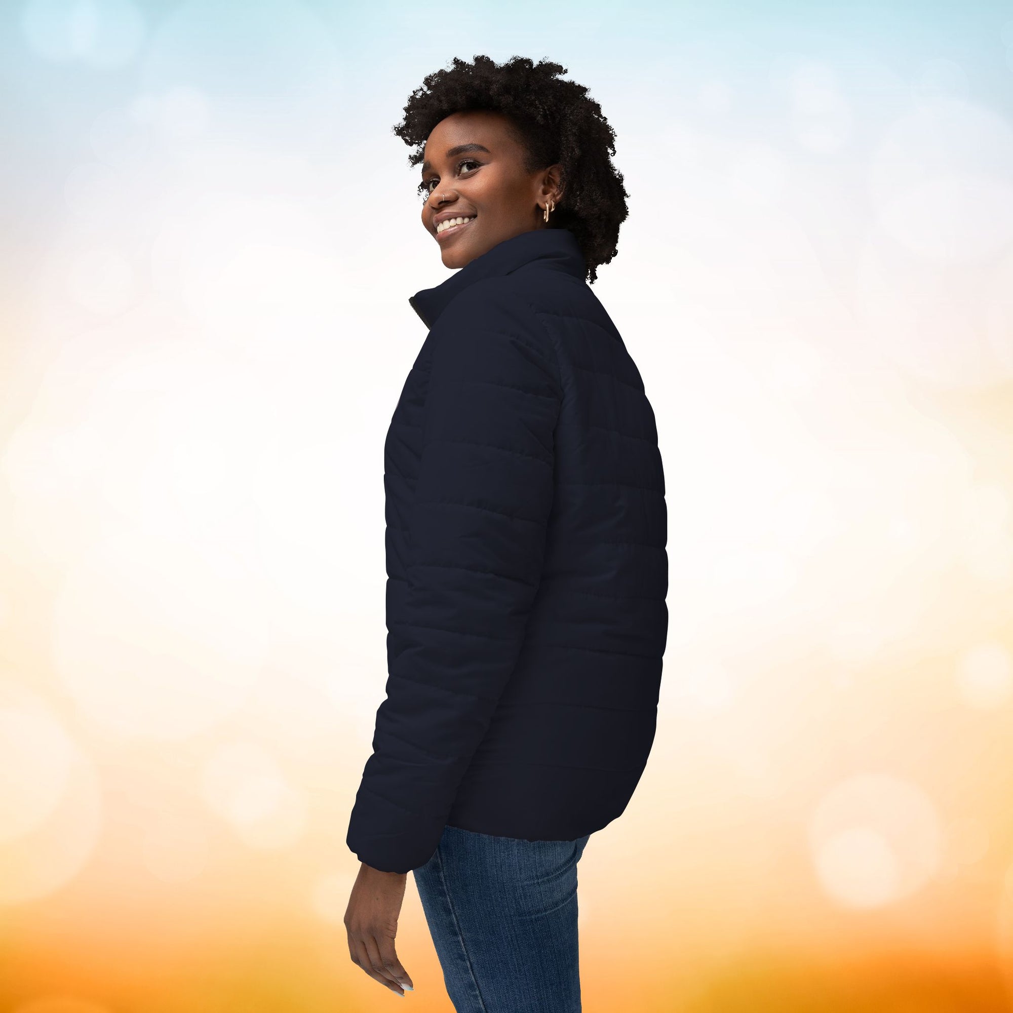 Das weibliche Model zeigt die linke Seite der Damen-Pufferjacke in einem Black Pearl Ton. Die Jacke ist horizontal gesteppt, hat eine glatte Oberfläche, einen hohen Stehkragen und einen durchgehenden Reißverschluss. Designed, by Just a Girl