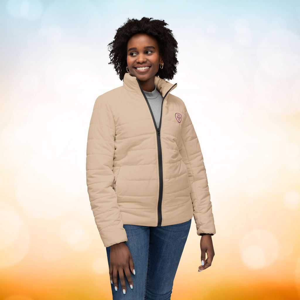 Ein weibliches Model zeigt die Damen-Pufferjacke von vorne in einem Brown Sugar Farbton. Die Jacke ist horizontal gesteppt, hat eine glatte Oberfläche, einen hohen Stehkragen und einen durchgehenden Reißverschluss. designed, by Just a Girl.

