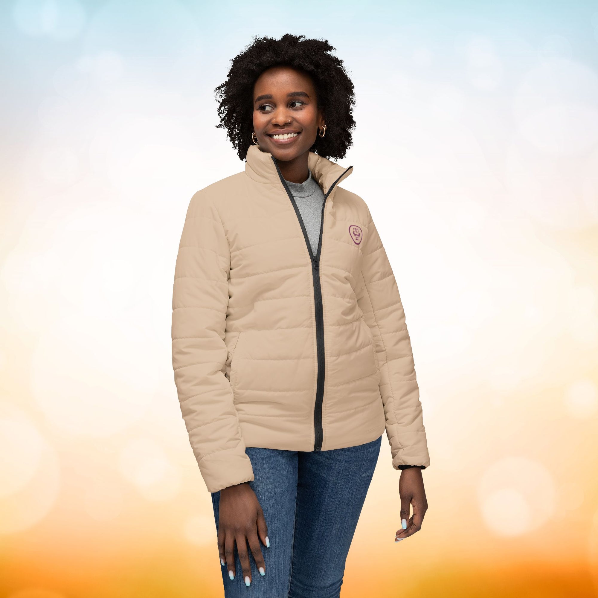 Ein weibliches Model zeigt die Damen-Pufferjacke von vorne in einem Brown Sugar Farbton. Die Jacke ist horizontal gesteppt, hat eine glatte Oberfläche, einen hohen Stehkragen und einen durchgehenden Reißverschluss. designed, by Just a Girl.

