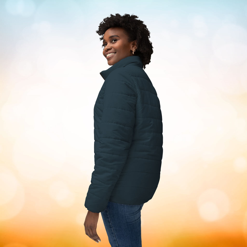 Ein weibliches Model zeigt mit der Seitenansicht eine Damen-Pufferjacke in einem Red Brass Farbton. Die Jacke ist horizontal gesteppt, hat eine glatte Oberfläche, einen hohen Stehkragen und einen durchgehenden Reißverschluss. Designed, by Just a Girl