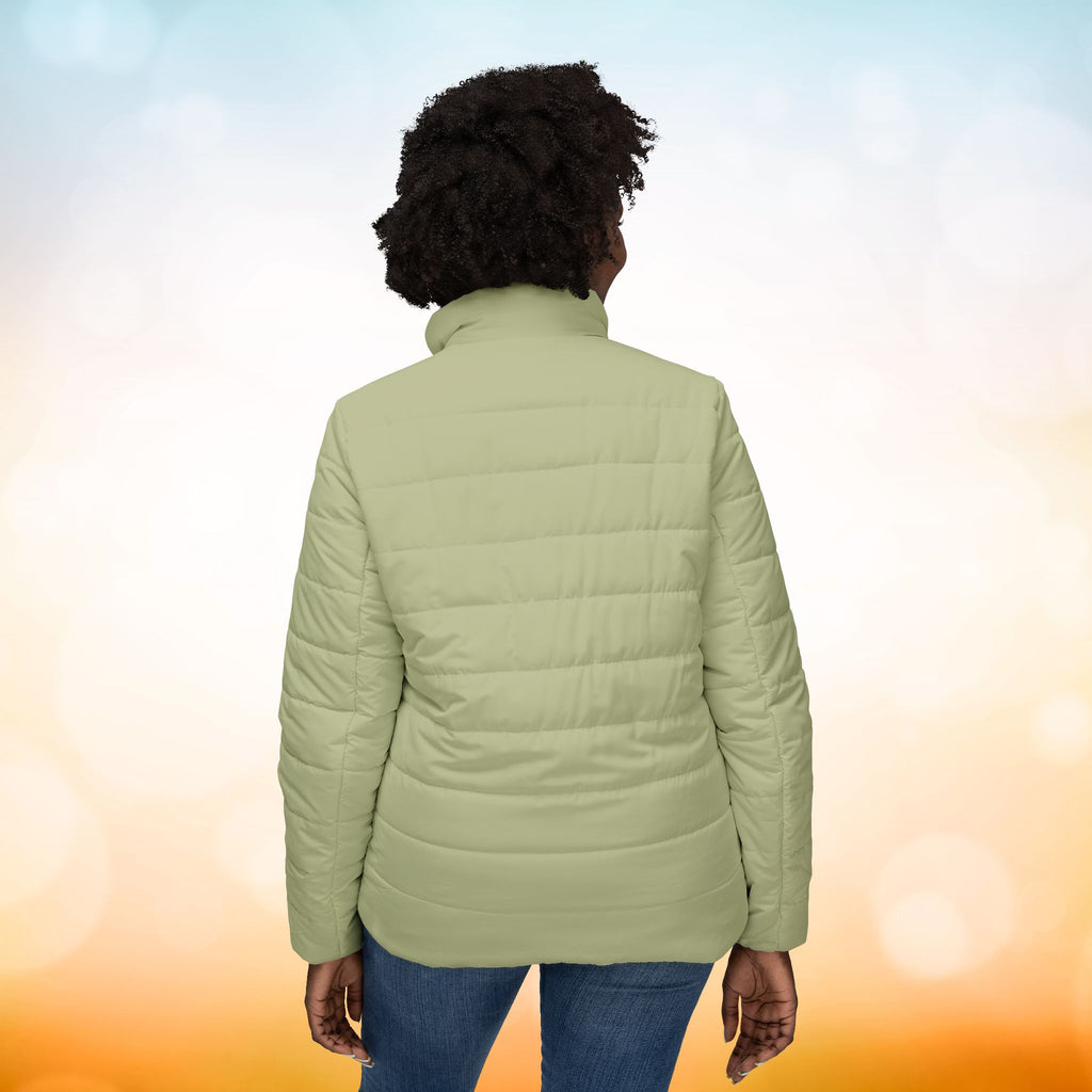 Ein weibliches Model trägt eine Damen-Pufferjacke in Sage Green. Das Model zeigt sich von der Rückenansicht. Die Jacke ist horizontal gesteppt, hat eine glatte Oberfläche sowie einen hohen Stehkragen. Designed, by Just a Girl.