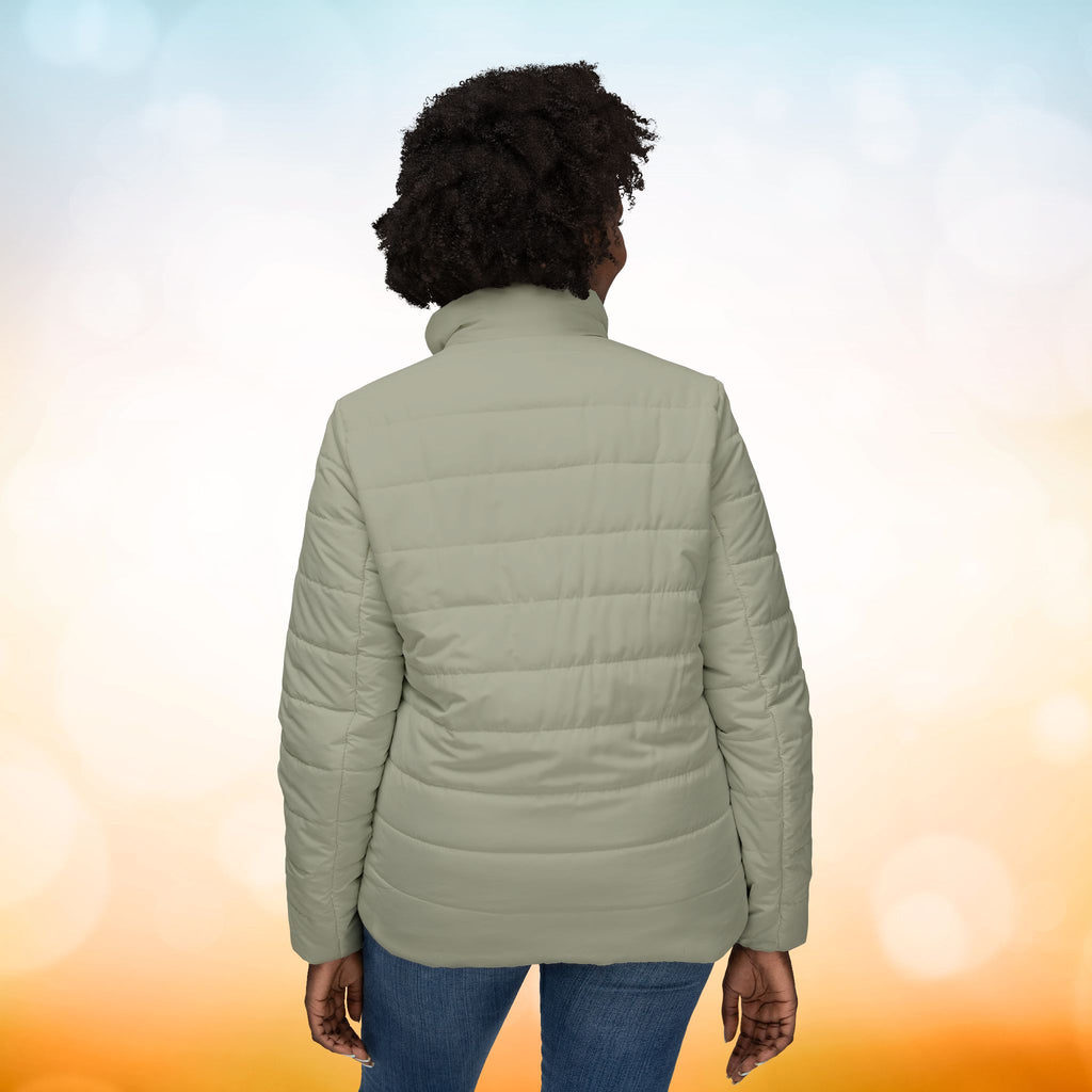  Ein weibliches Model trägt eine  Damen-Pufferjacke Ansicht von hinten in einem Ash Grey Farbton. Die Jacke ist horizontal gesteppt, hat eine glatte Oberfläche sowie einen hohen Stehkragen. Designed, by Just a Girl