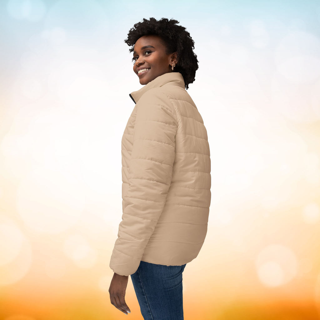 Ein weibliches Model zeigt die Damen-Pufferjacke von der linken Seite in einem Brown Sugar Farbton. Die Jacke ist horizontal gesteppt, hat eine glatte Oberfläche, einen hohen Stehkragen und einen durchgehenden Reißverschluss. designed, by Just a Girl.

