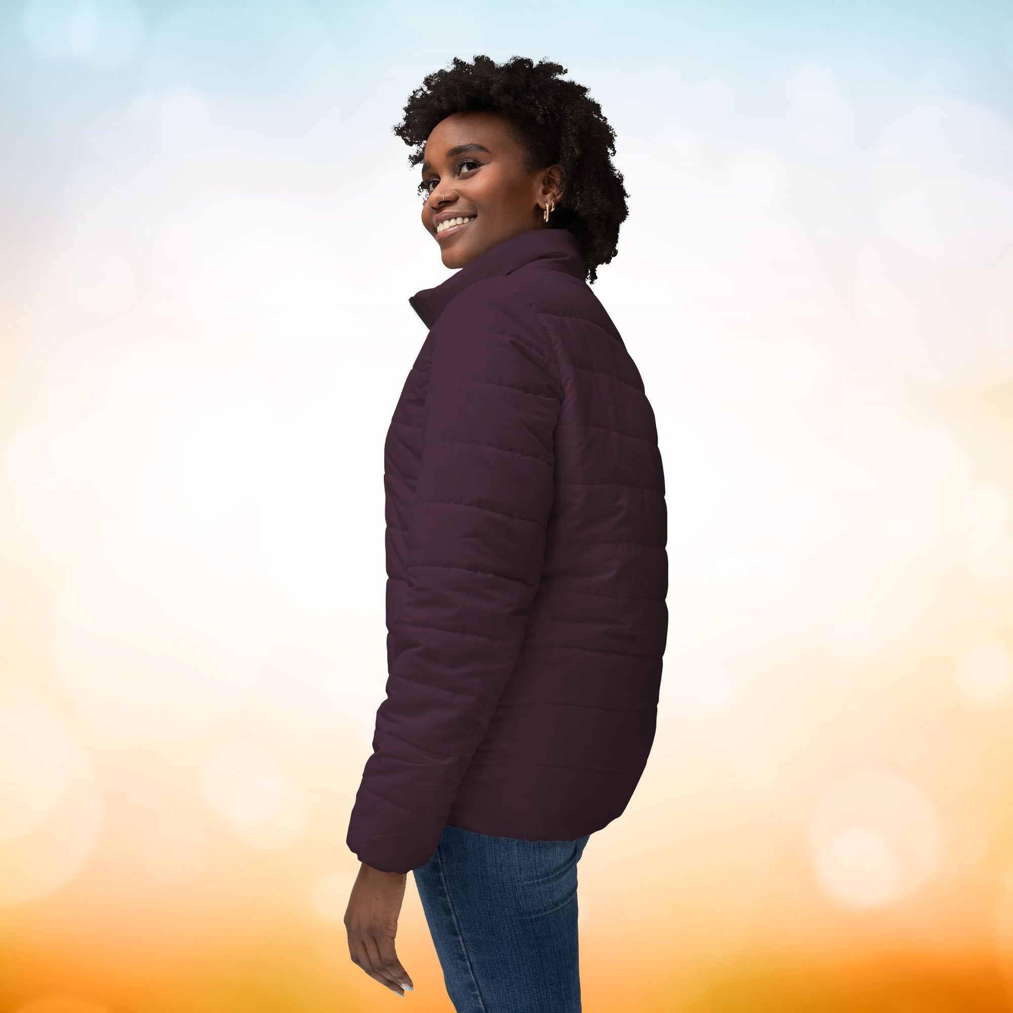 Ein weibliches Model zeigt von der linken Seite eine Damen-Pufferjacke in einem Dark Plum Farbton. Die Jacke ist horizontal gesteppt, hat eine glatte Oberfläche, einen hohen Stehkragen und einen durchgehenden Reißverschluss. Designed, by Just a Girl

