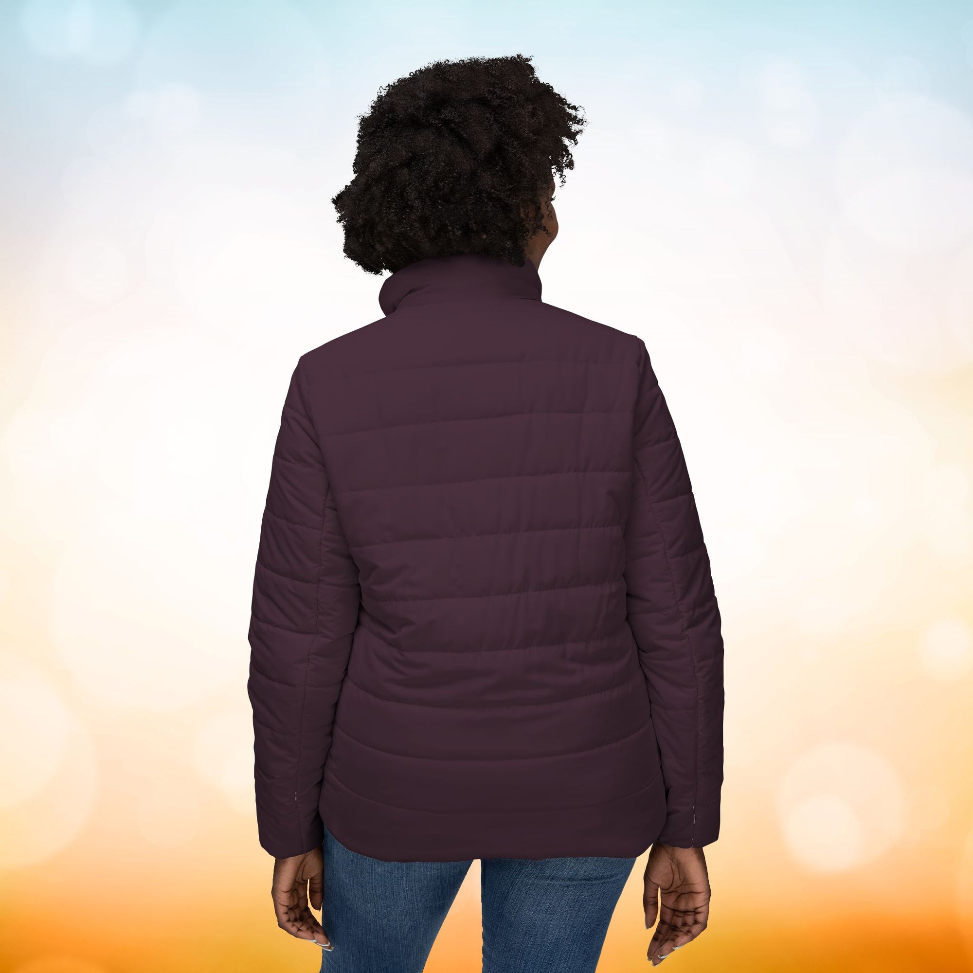 Ein weibliches Model zeigt von hinten eine Damen-Pufferjacke in einem Dark Plum Farbton. Die Jacke ist horizontal gesteppt, hat eine glatte Oberfläche sowie einen hohen Stehkragen. Designed, by Just a Girl

