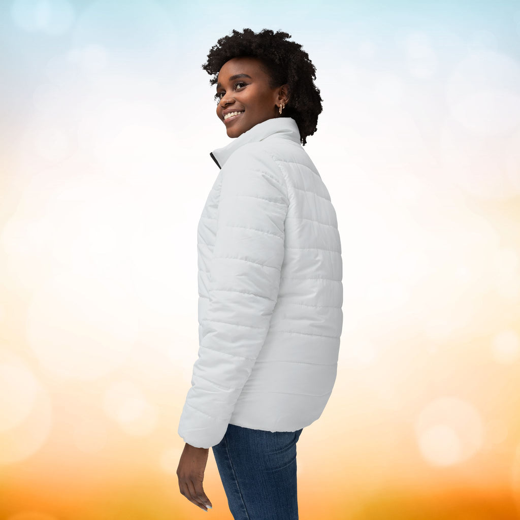 Ein weibliches Model zeigt sich von der linken Seitenansicht mit einer Damen-Pufferjacke  in einem Ivory Farbton. Die Jacke ist horizontal gesteppt, hat eine glatte Oberfläche, einen hohen Stehkragen und einen durchgehenden Reißverschluss. Designed, by Just a Girl

