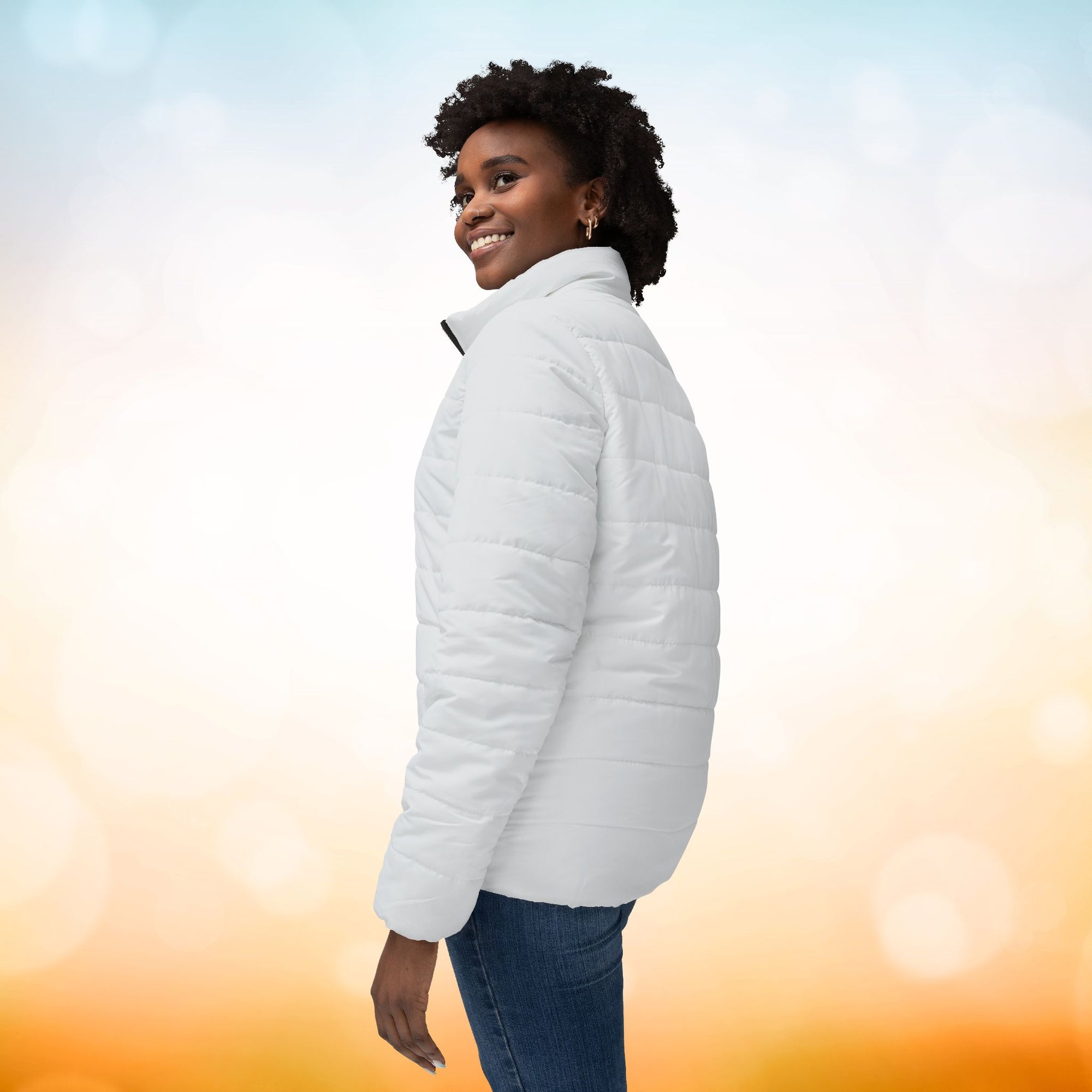 Ein weibliches Model zeigt sich von der linken Seitenansicht mit einer Damen-Pufferjacke  in einem Ivory Farbton. Die Jacke ist horizontal gesteppt, hat eine glatte Oberfläche, einen hohen Stehkragen und einen durchgehenden Reißverschluss. Designed, by Just a Girl

