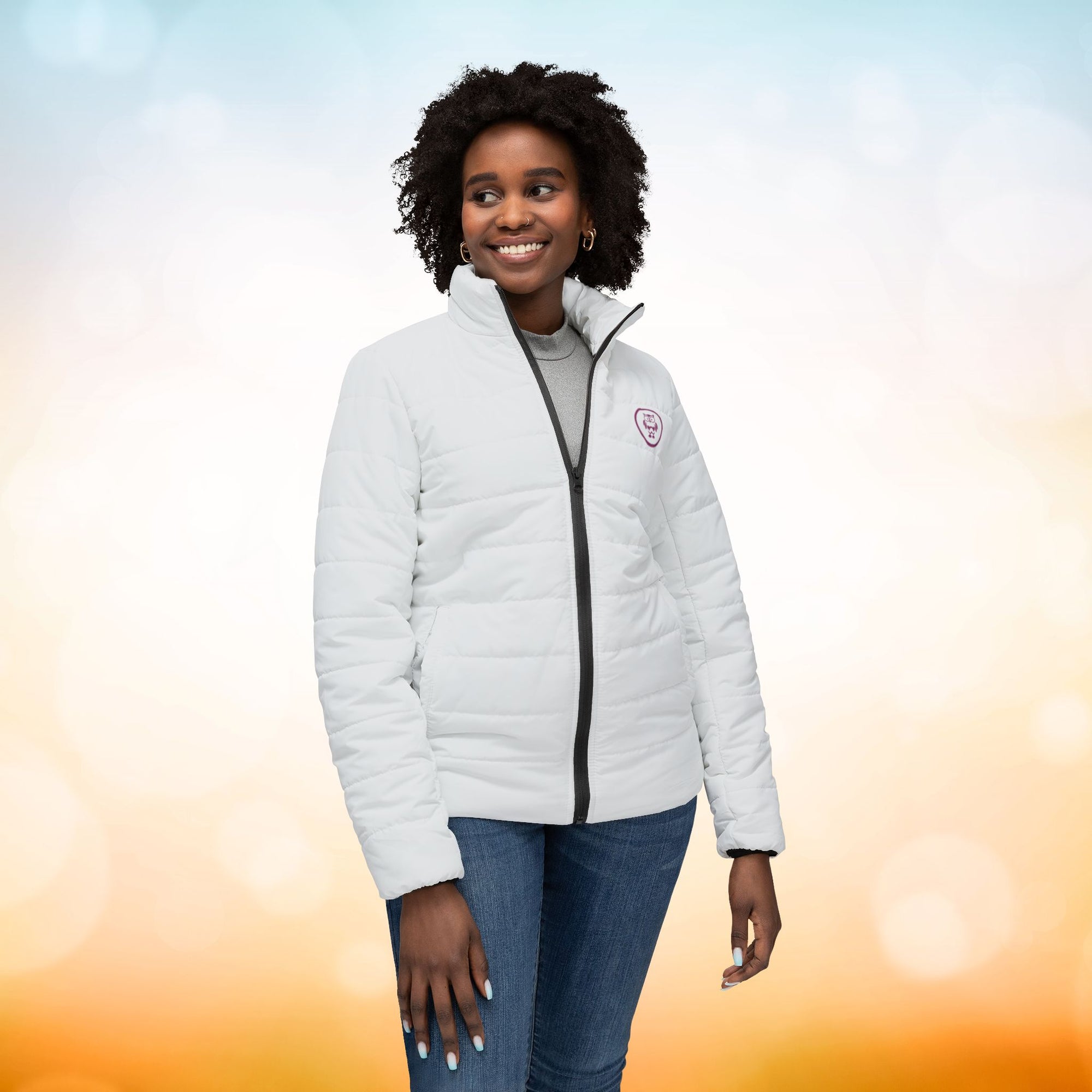 Ein weibliches Model zeigt sich von der Voderansicht mit einer Damen-Pufferjacke  in einem Ivory Farbton. Die Jacke ist horizontal gesteppt, hat eine glatte Oberfläche, einen hohen Stehkragen und einen durchgehenden Reißverschluss. Designed, by Just a Girl

