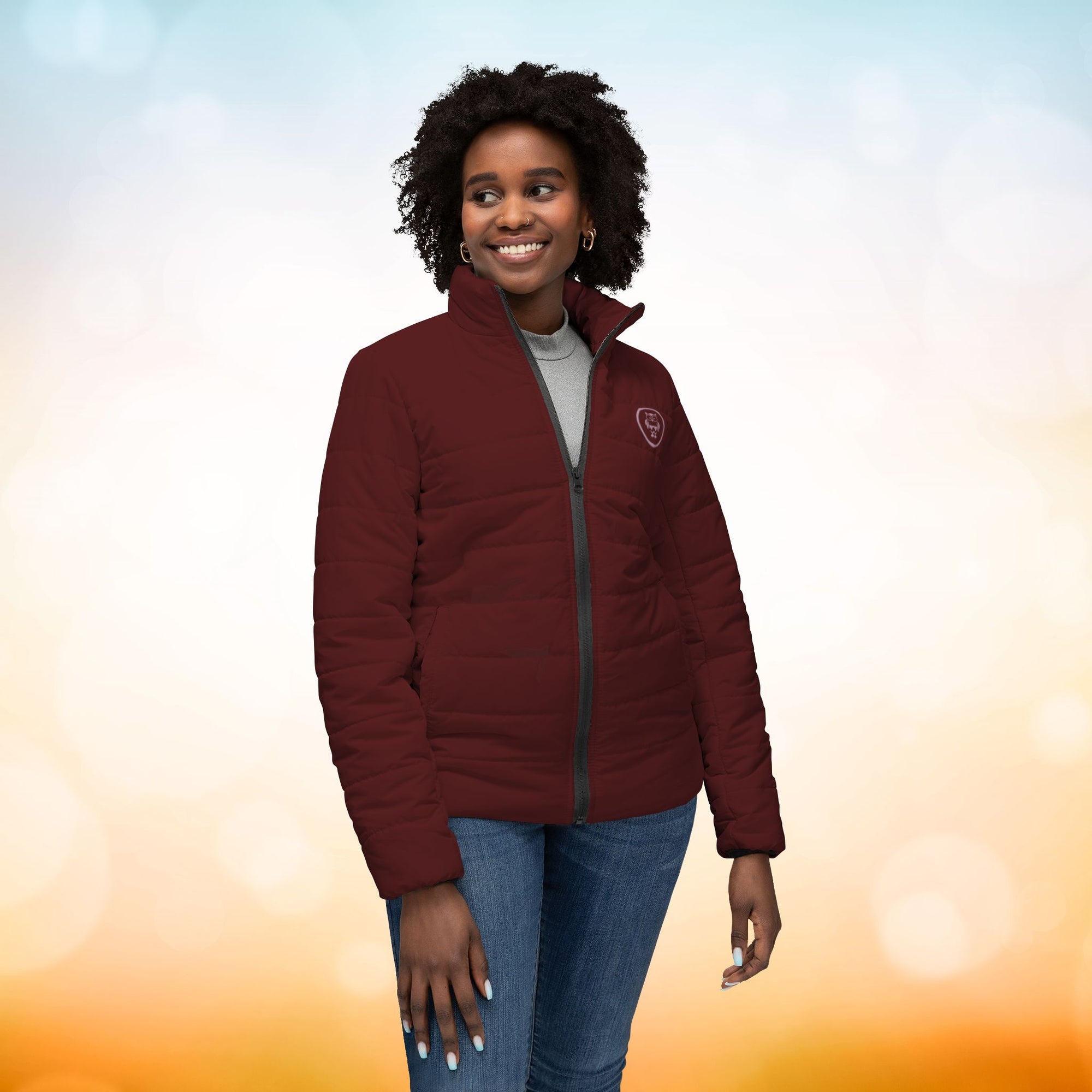 Ein weibliches Model trägt eine Damen-Pufferjacke in der Vorderansicht in einem Oxblood Farbton. Die Jacke ist horizontal gesteppt, hat eine glatte Oberfläche, einen hohen Stehkragen und einen durchgehenden Reißverschluss. Designed, by Just a Girl.

