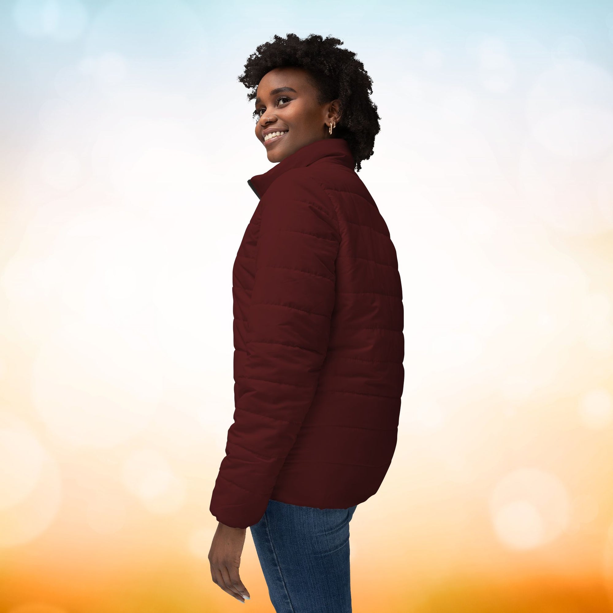 Ein weibliches Model trägt eine Damen-Pufferjacke in der Seitenansicht in einem Oxblood Farbton. Die Jacke ist horizontal gesteppt, hat eine glatte Oberfläche sowie einen hohen Stehkragen. Designed, by Just a Girl.

