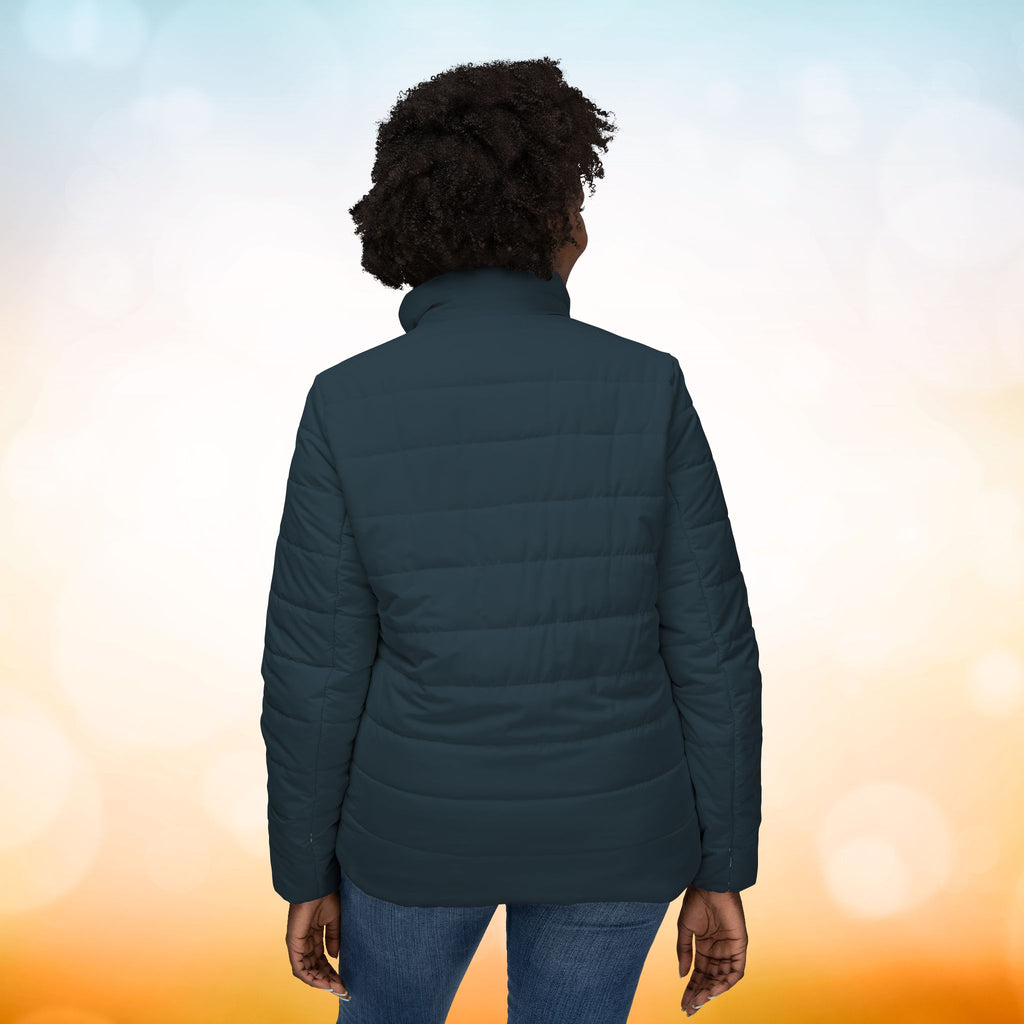 Ein weibliches Model zeigt mit der Rückenansicht eine Damen-Pufferjacke in einem Red Brass Farbton. Die Jacke ist horizontal gesteppt, hat eine glatte Oberfläche sowie einen hohen Stehkragen. Designed, by Just a Girl