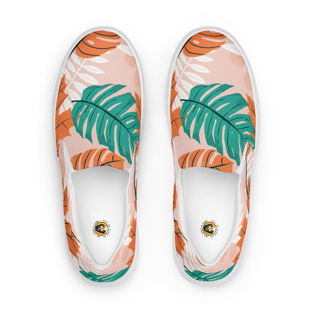 Ein Paar Damen Slip-on-Schuhe mit einem Blättermuster in Grün, scharfem Orange und Weiß auf einem pastellorangen Hintergrund. Die  Ansicht der Schuhe ist von oben vor einem weißen Hintergrund. Designed, by Just a Girl