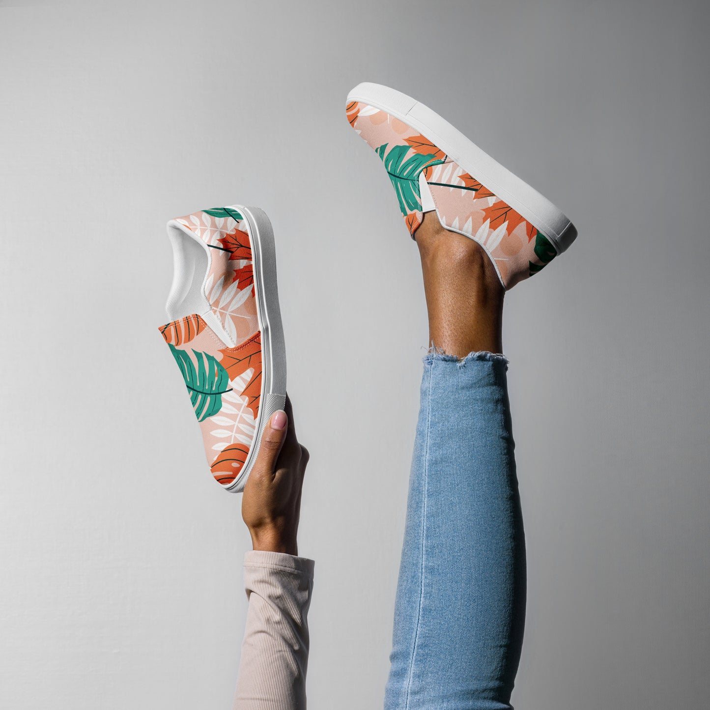 Ein weibliches Model zeigt tragend ein Bein in die Luft gestreckt und mit der anderen Hand den 2. Schuh zeigend  mit einem Blättermuster in Grün, herbsltichen Orange und Weiß auf einem pastell farbenen orangen Hintergrund. Designed, by Just a Girl.