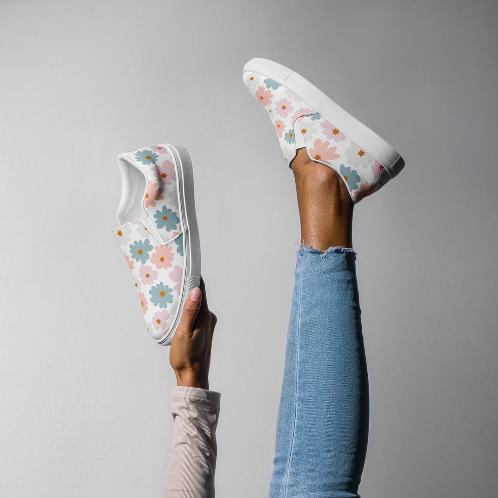 Ein weibliches Model zeigt tragend mit eine Bein in die Luft gestreckt und mit der anderen Hand haltend den anderen Schuh
die weißen Slip-on-Schuhe mit einem Muster aus pastellfarbenen Blüten in Hellblau und Zartrosa. Designed, by Just a Girl.