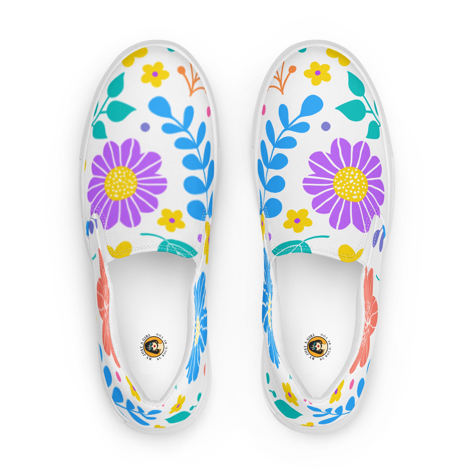 Ein Paar weiße Damen-Slip-on-Schuhe mit einem Muster aus bunten, stilisierten Blumen in Rot, Lila, Gelb, Grün und Blau. Die Schuhe zeigt die Ansicht von oben vor einem weißen Hintergrund. Designed, by Just a Girl.