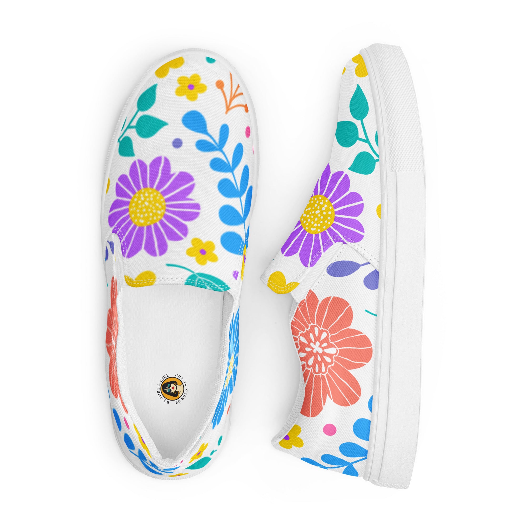 Ein Paar weiße Damen-Slip-on-Schuhe mit einem Muster aus bunten, stilisierten Blumen in Rot, Lila, Gelb, Grün und Blau. Die Schuhe werden von oben und seitlich angezeigt vor einem weißen Hintergrund. Designed, by Just a Girl