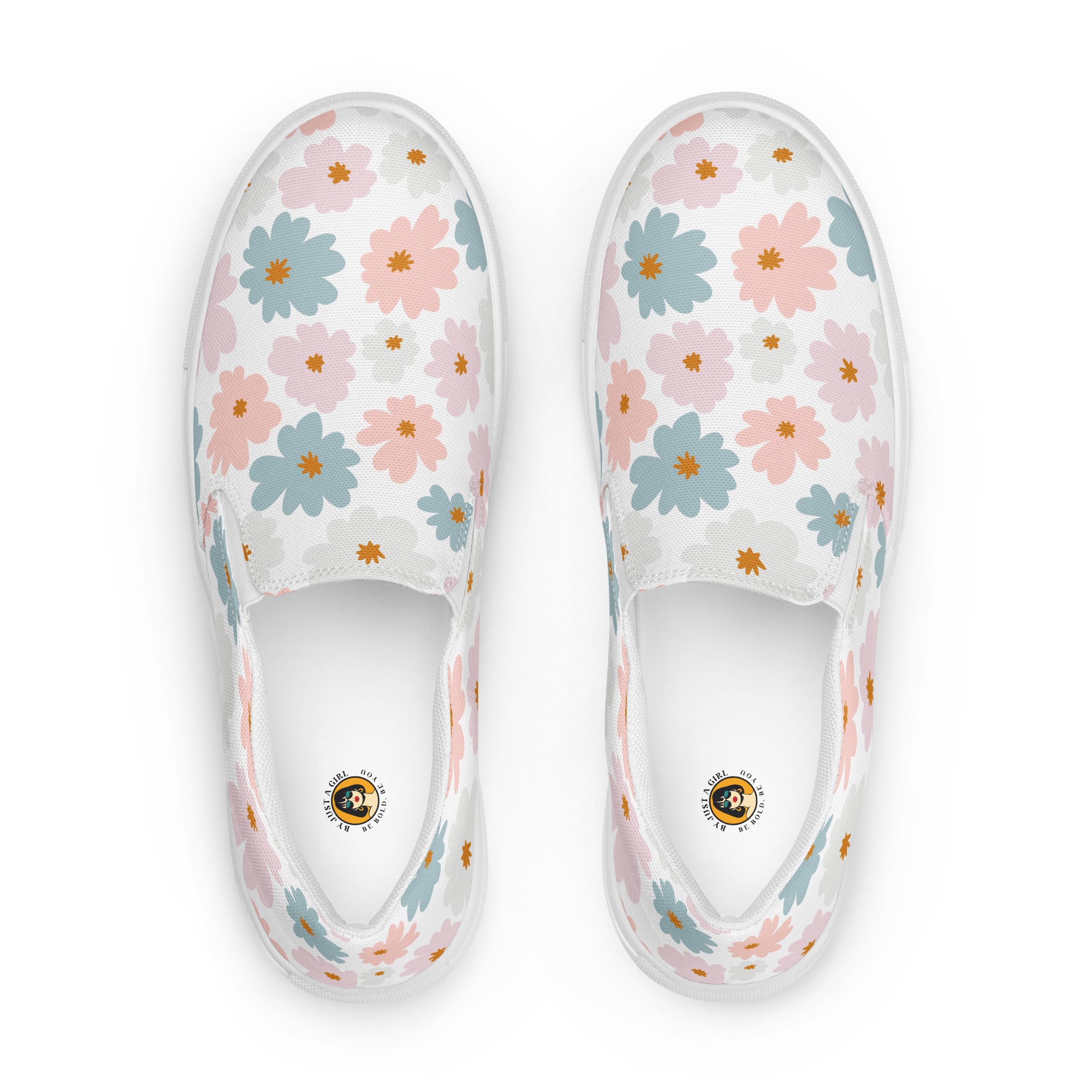 Ein Paar weiße Damen-Slip-on-Schuhe mit einem Muster aus pastellfarbenen Blüten in Hellblau und Zartrosa. Die Schuhe werden von der Ansicht von oben  vor einem weißen Hintergrund gezeigt. Designed, by Just a Girl.