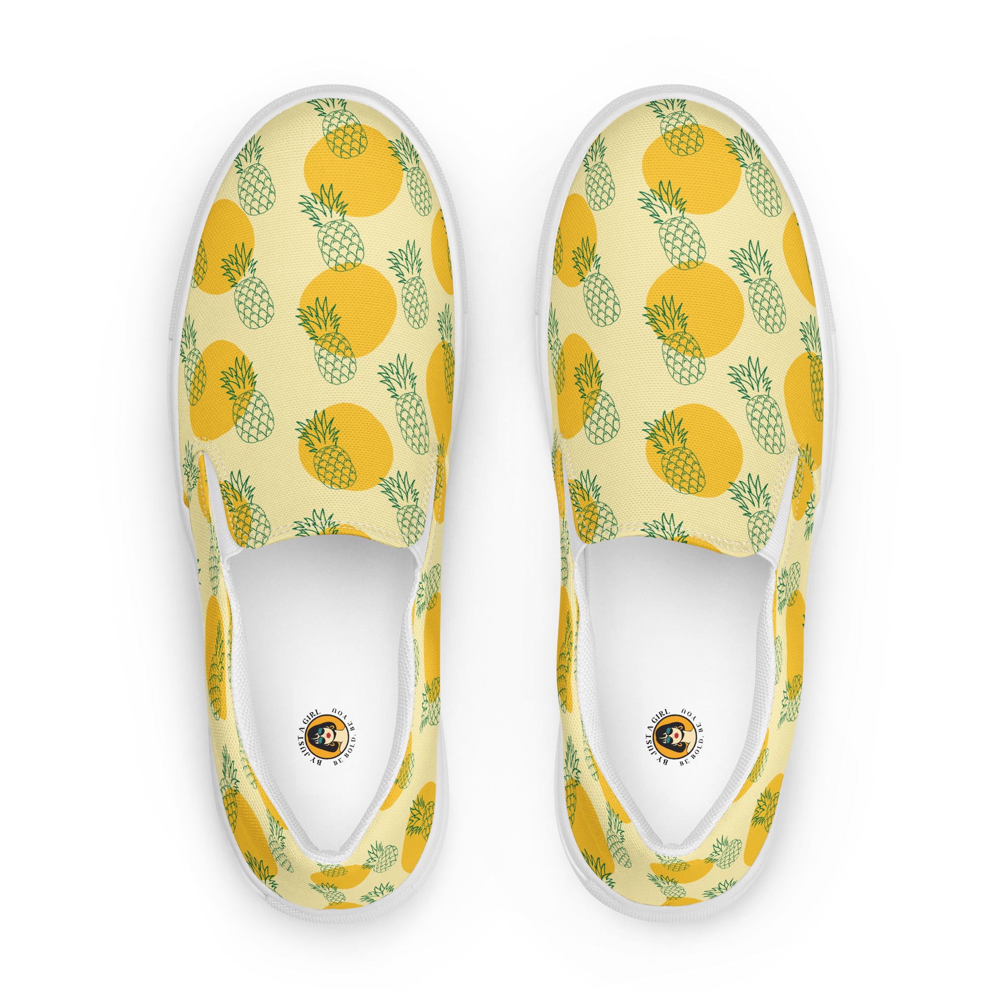 Ein Paar Damen Slip-on-Schuhe mit einem Muster aus grünen Ananas-Outlines und orangen Kreisen auf gelben Hintergrund. Die Ansicht der Schuhe ist von oben vor einem weißen Hintergrund. Designed, by Just a Gir