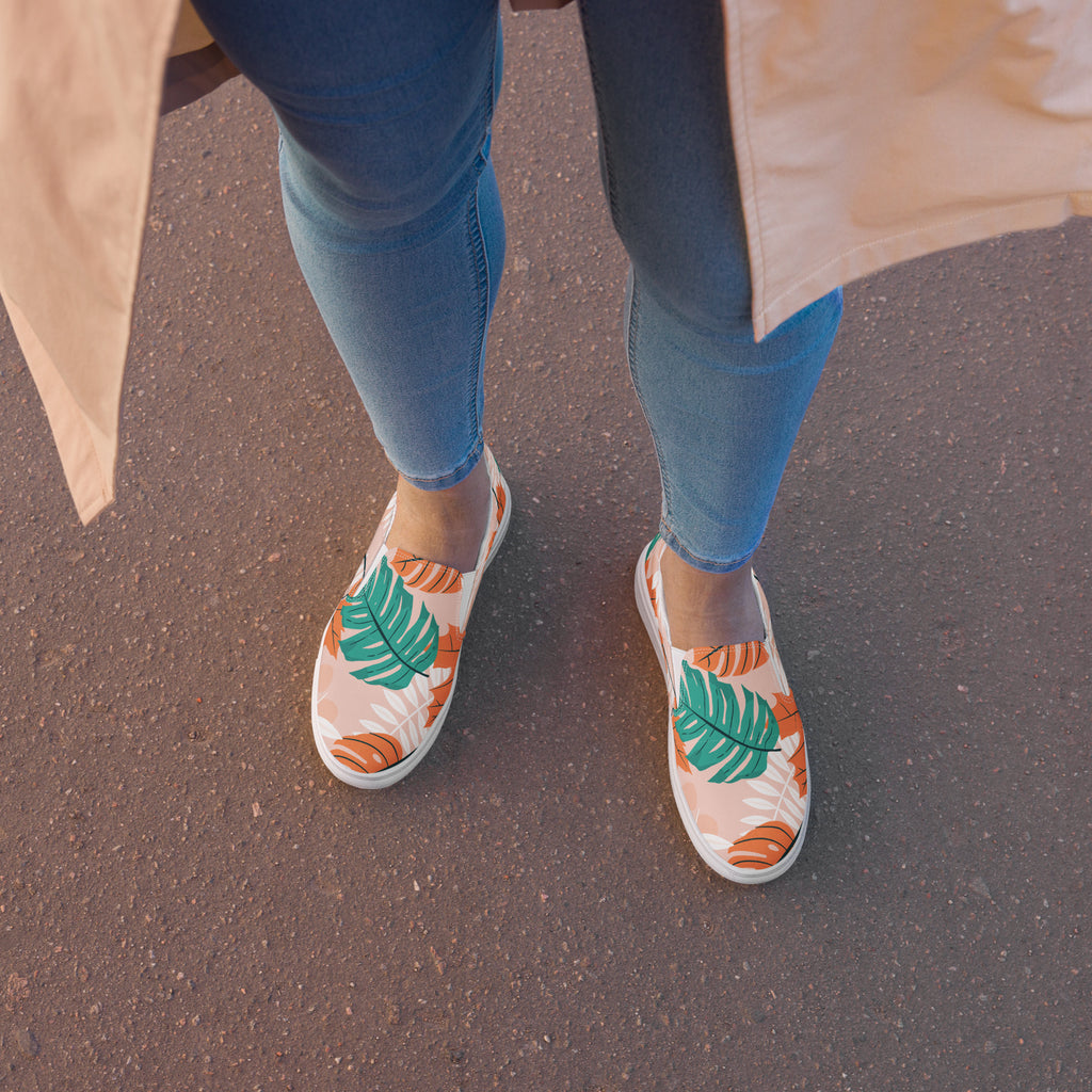 Ein weibliches Model zeigt tragend draßen die Slip Ons im Sitzen  mit einem Blättermuster in Grün, herbsltichen Orange und Weiß auf einem pastell farbenen orangen Hintergrund. Designed, by Just a Girl.