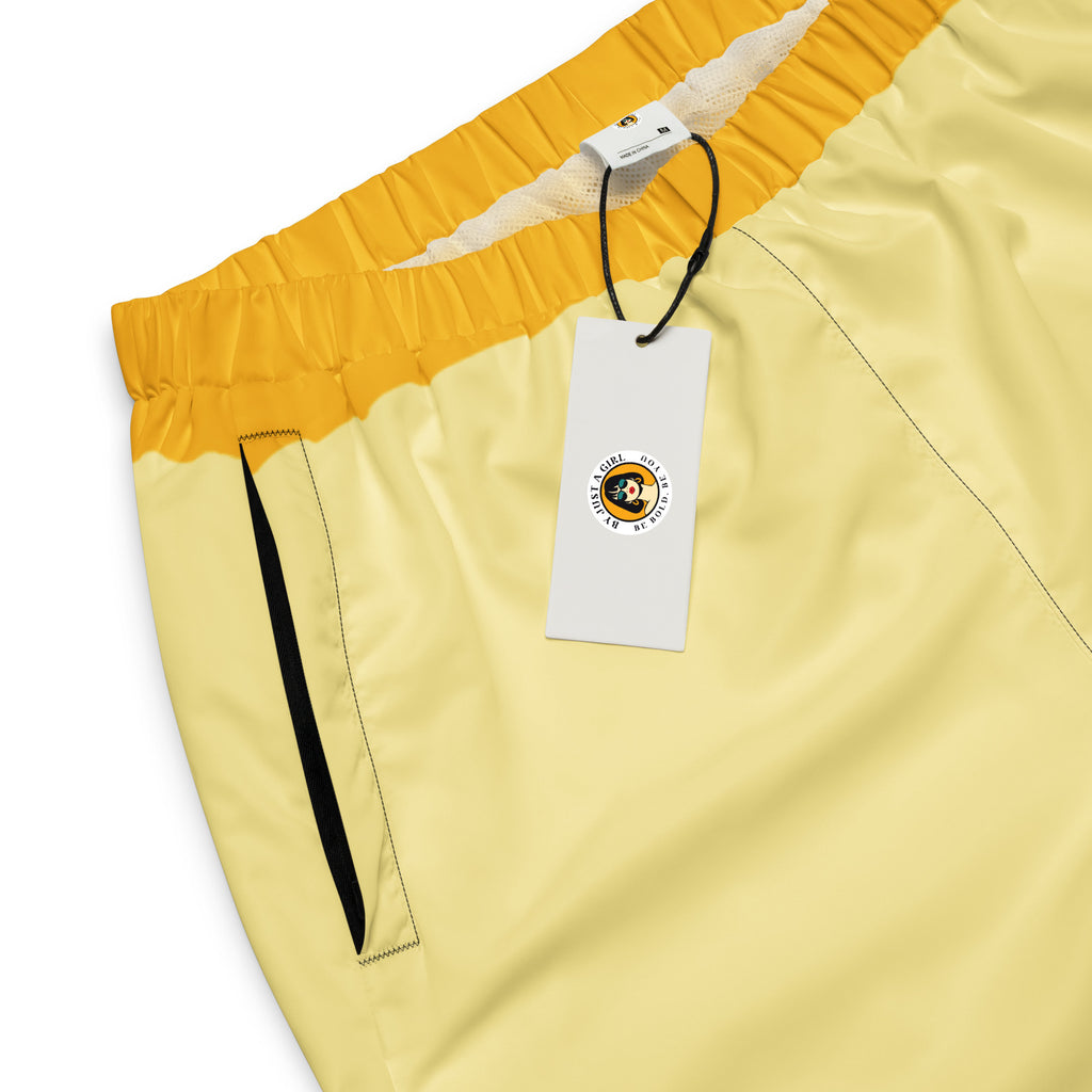 Damen Trainingshose in Gelb, Schwarz und einem pastell gelb, mit einem auffälligen schwarzen Punktemuster auf der unteren gelben Hälfte, mockup Hosenbundansicht mit Tasche & Logo vorne. By Just a Girl.