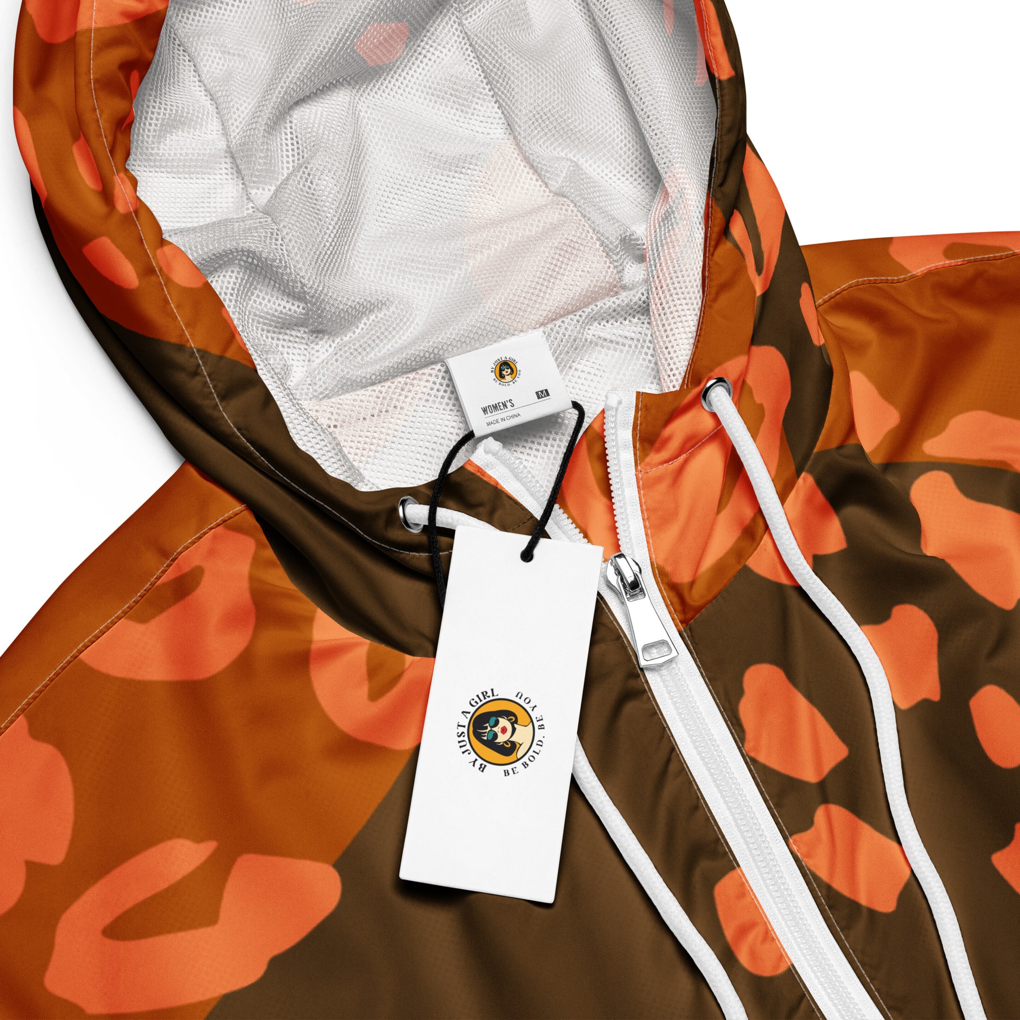 Ein Damen Cropped Windbreaker in Dunkelbraun und Orange mit einem abstrakten Muster aus unregelmäßigen Flecken und Formen, teilweise leopardenähnlich. Die Jacke hat eine Kapuze, einen halben Reißverschluss, schwarze Kordeln und einen verstellbaren Saum. Mockup Kapuzen Ansicht mit weißem Reisverschluß. By Just a Girl.