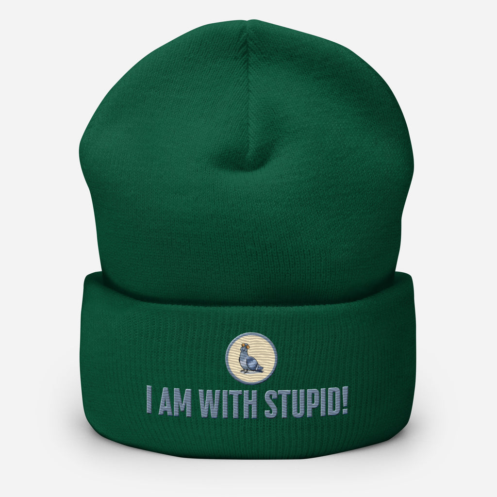 Eine Fichtengrüne Cuffed Beanie mit aufgesticktem Patch als Taube mit einem runden beige-grauen Rahmen auf der Vorderseite. Darunter ein Schriftzug mit Grossgeschriebenen Buchstaben "I Am with Stupid!" Designed, by Just a Girl.