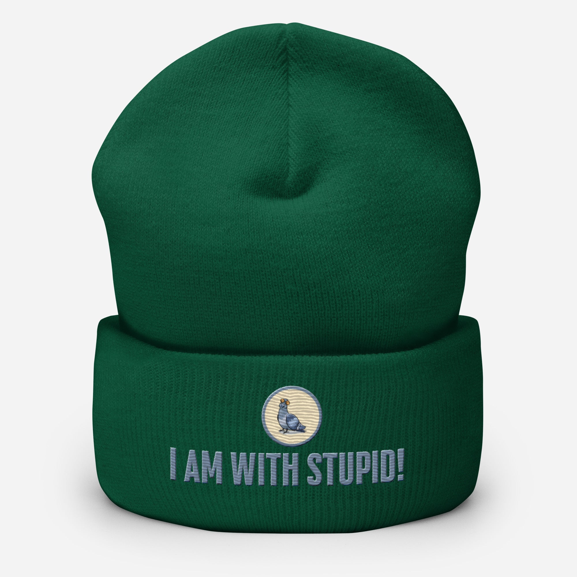 Eine Fichtengrüne Cuffed Beanie mit aufgesticktem Patch als Taube mit einem runden beige-grauen Rahmen auf der Vorderseite. Darunter ein Schriftzug mit Grossgeschriebenen Buchstaben "I Am with Stupid!" Designed, by Just a Girl.