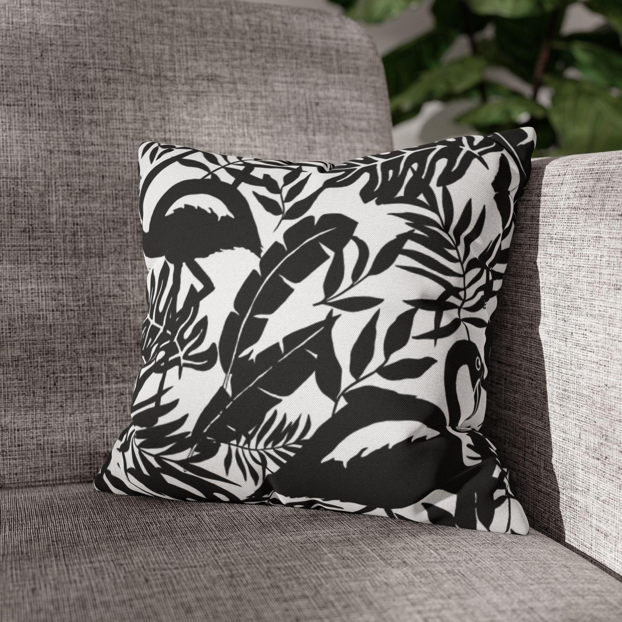 Einzelne Ansicht des Flamingo Jungle Kissens auf einem grauen Sofa mit einer Monstera Pflanze im Hintergrund.