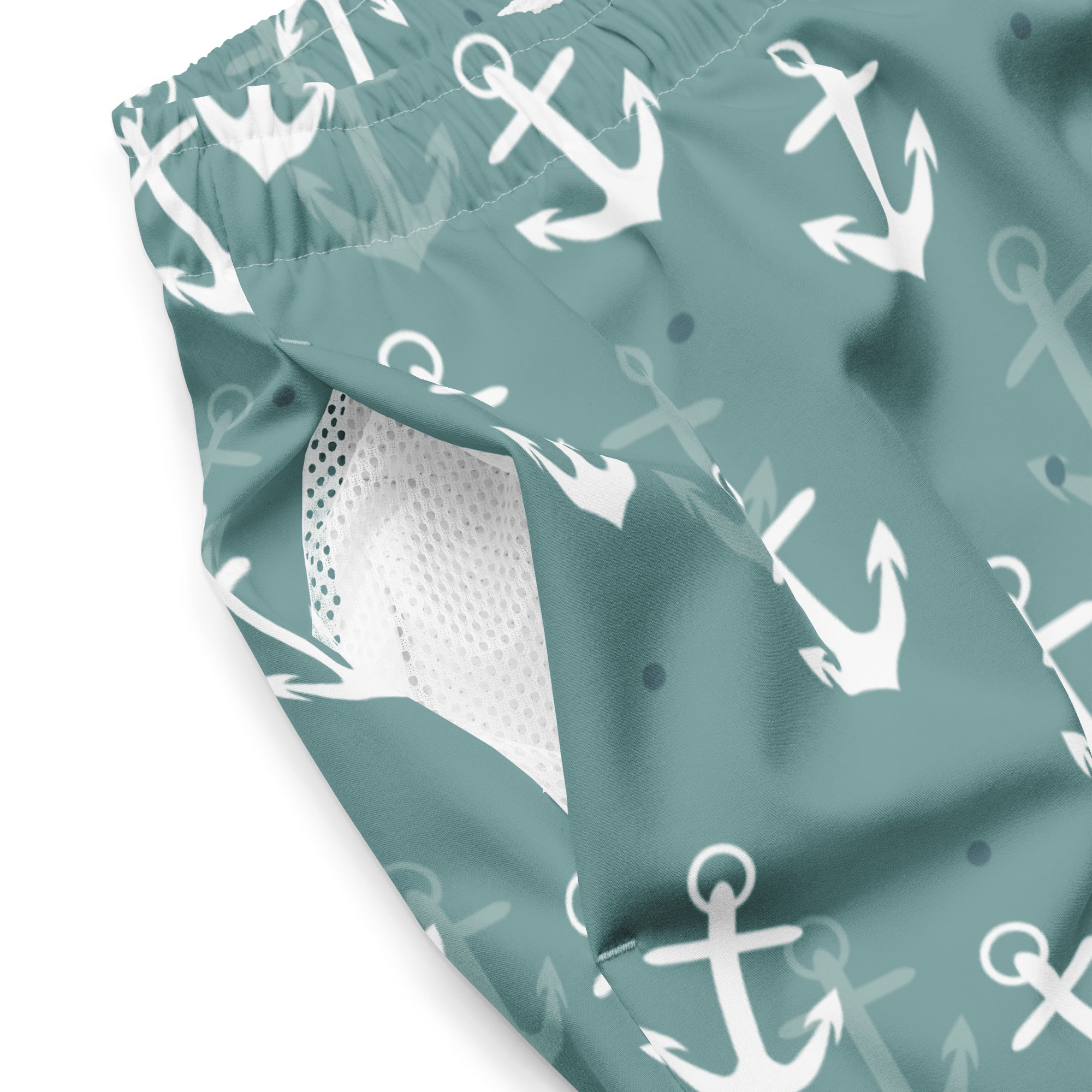 Eine Badeshorts in einem gedeckten Türkis- oder Blauton mit einem wiederkehrenden Muster aus weißen und hellgrauen Ankern und kleinen blauen Punkten. Der Bund ist elastisch und farblich passend.