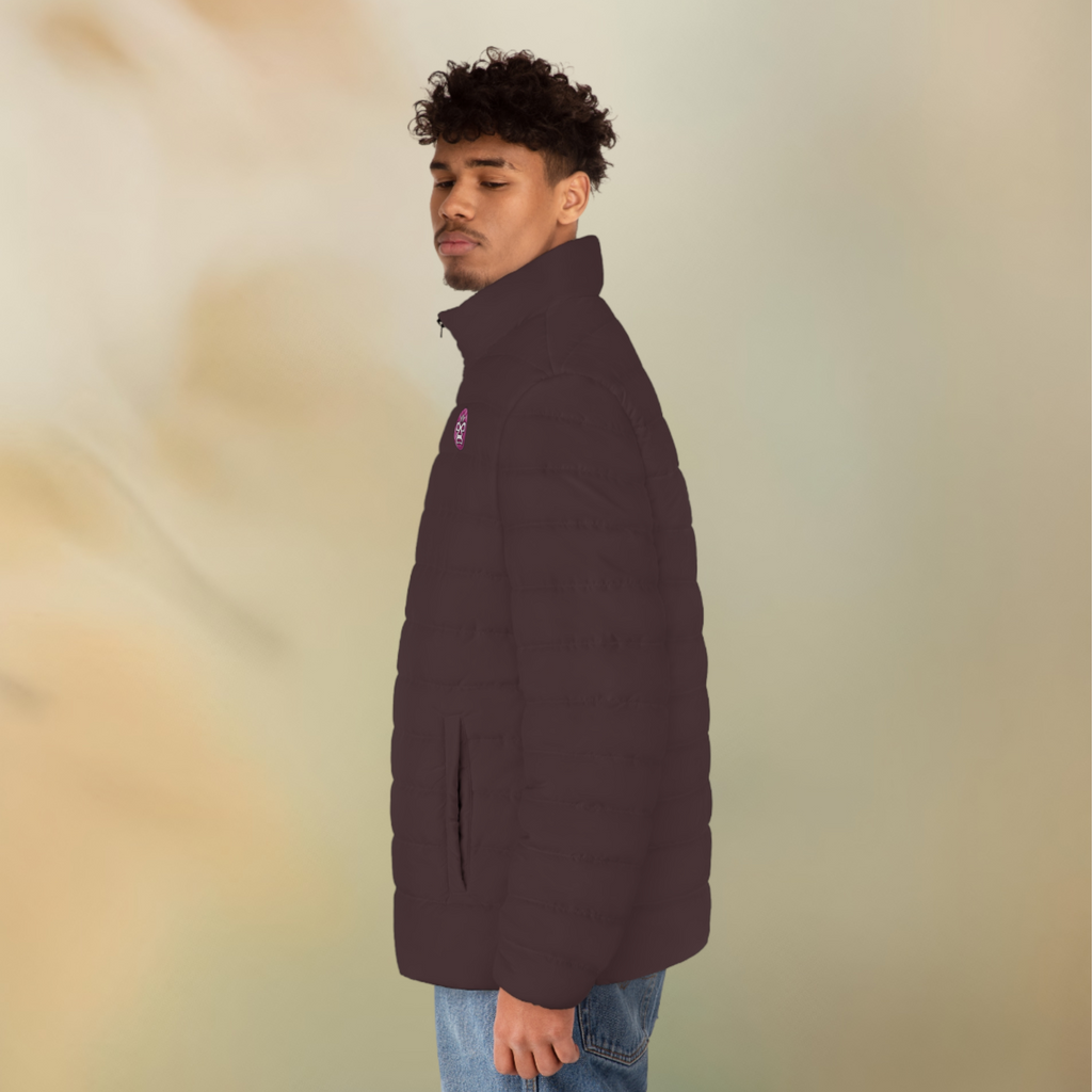 Ein männliches Model zeigt tragend die Herren-Pufferjacke von der linken Seitenansicht in einem Schokoladenbraunen Farbton. Die Jacke ist horizontal gesteppt, hat eine glatte Oberfläche, einen hohen Stehkragen und einen durchgehenden Reißverschluss in schwarz. Die Jacke hat auf der linken Brust ein Maori Emblem.  Designed, by Just a Girl

