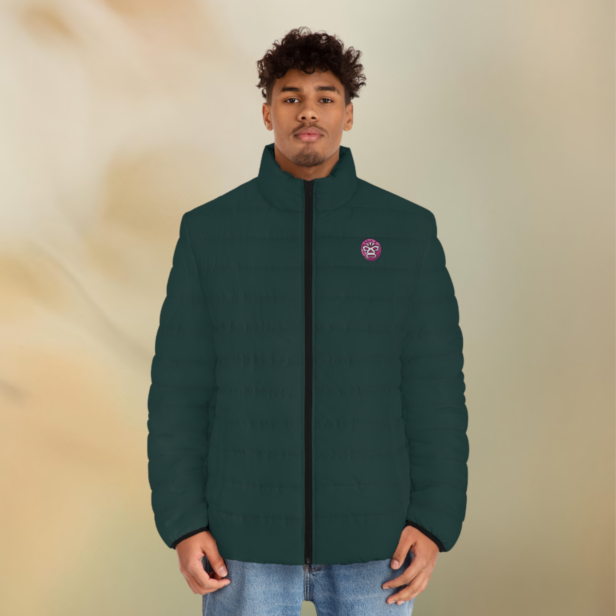 Ein männliches Model zeigt tragend die  Herren-Pufferjacke Vorderansicht in einem Tiefen Tafel Farbton. Die Jacke ist horizontal gesteppt, hat eine glatte Oberfläche, einen hohen Stehkragen und einen durchgehenden Reißverschluss der Schwarz ist . Auf der linken Brusthöhe ist ein Emblem im Maori Stil. Designed, by Just a Girl