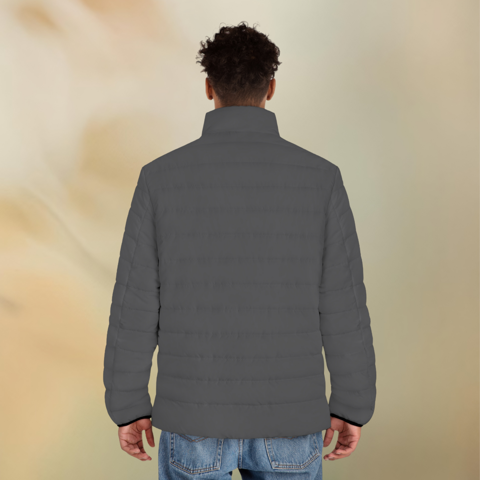 Ein männliches Model zeigt tragend von der Rückseite die Herren-Pufferjacke in einem Grey Stone Farbton. Die Jacke ist horizontal gesteppt, hat eine glatte Oberfläche sowie einen hohen Stehkragen. Designed, by Just a Girl

