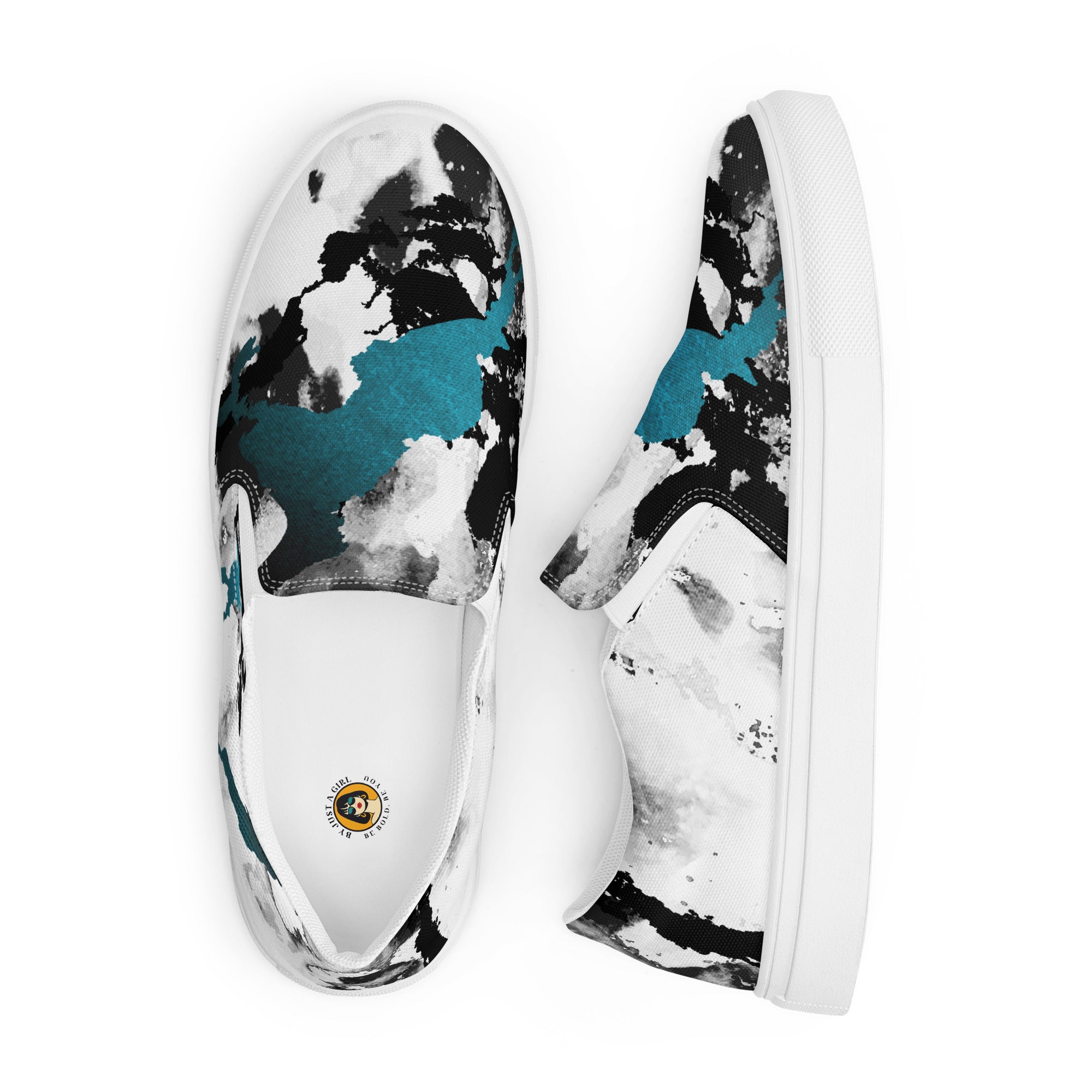 Ein Paar weißer Slip-On Canvas Schuhe mit einem abstrakten Muster aus großen, unregelmäßigen Klecksen und Flecken in Schwarz, Grau und leuchtendem Türkis. Die Sohle ist weiß. Die Schuhe sind leicht nach links gedreht, sodass die Vorderseite beider Schuhe sichtbar ist.