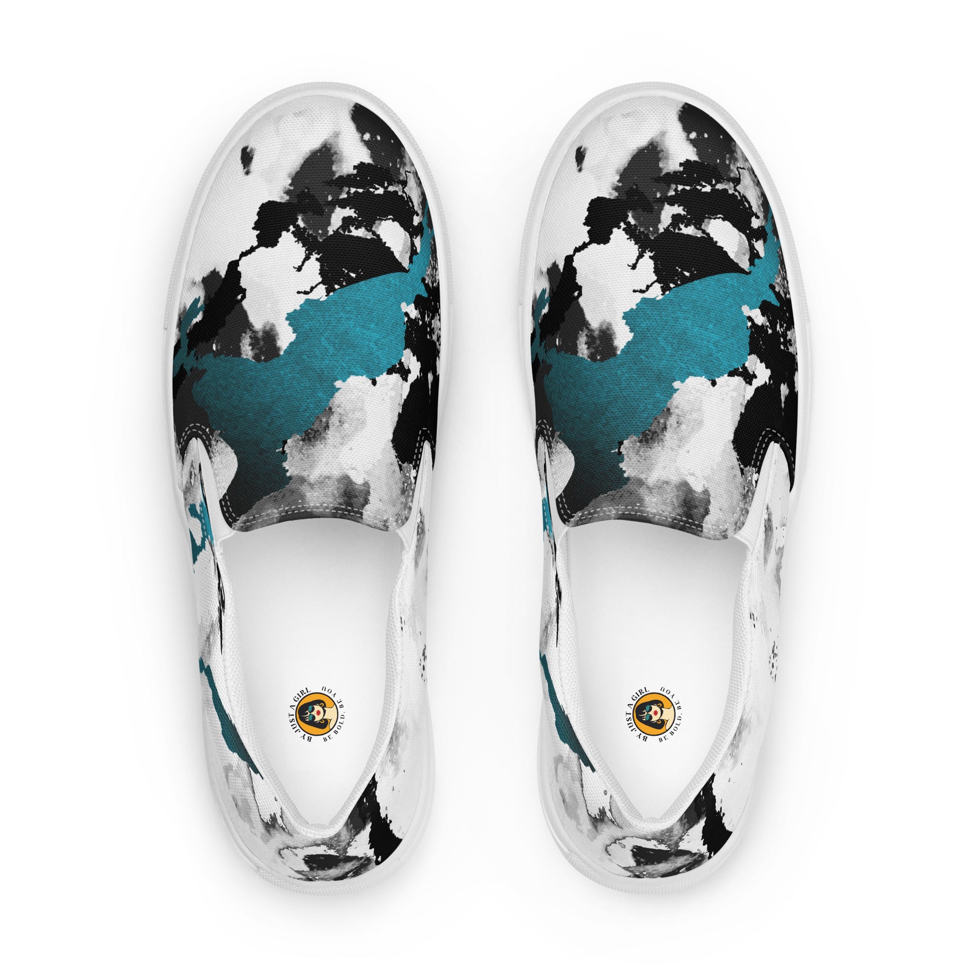 Ein Paar weißer Slip-On Canvas Schuhe mit einem abstrakten Muster aus großen, unregelmäßigen Klecksen und Flecken in Schwarz, Grau und leuchtendem Türkis. Die Sohle ist weiß. Die Schuhe sind leicht nach links gedreht, sodass die Vorderseite beider Schuhe sichtbar ist.