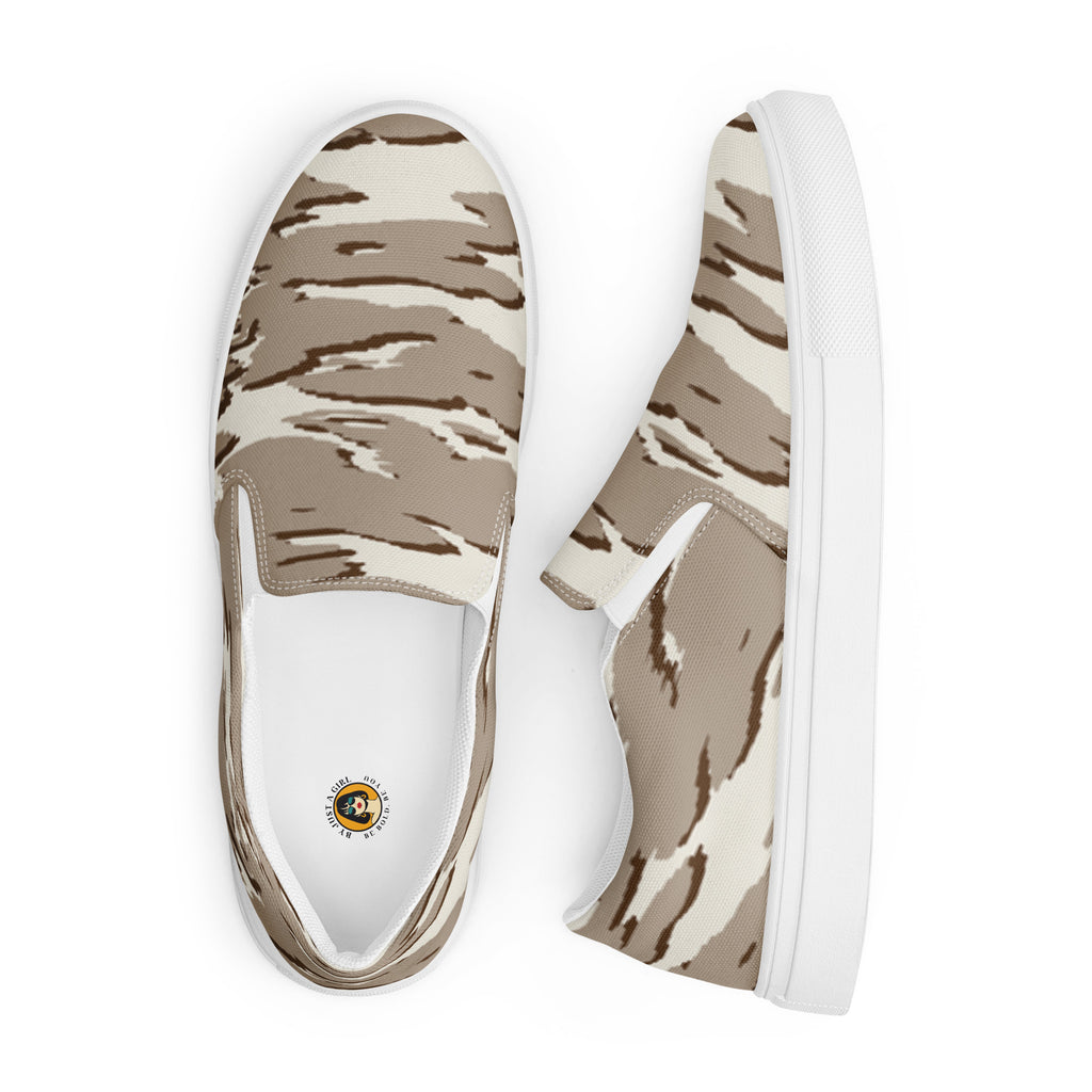 Ein Paar beiger Slip-On Canvas Schuhe mit einem wellenförmigen Camouflage-Muster in Hellbeige und Dunkelbeige. Die Sohle ist weiß. Die Schuhe sind leicht nach links gedreht, sodass die Vorderseite beider Schuhe sichtbar ist.