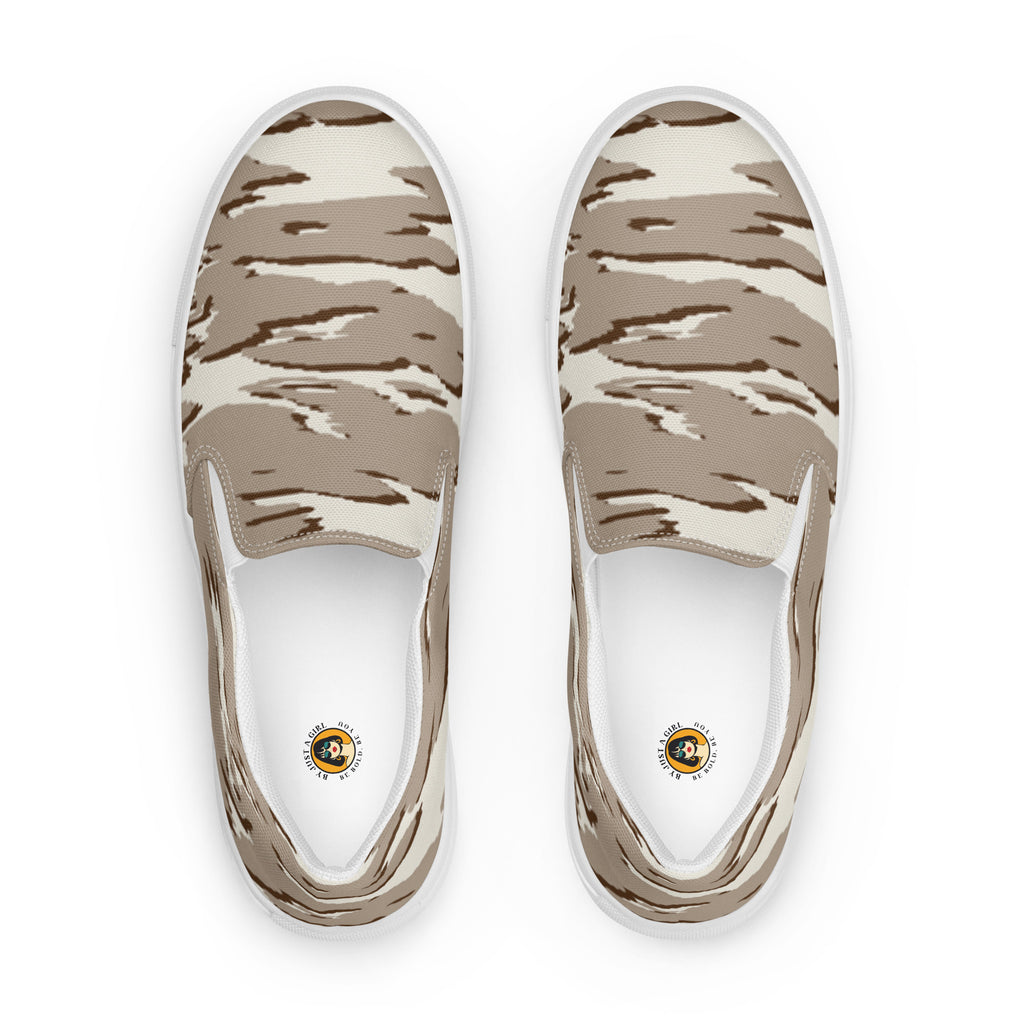 Ein Paar beiger Slip-On Canvas Schuhe mit einem wellenförmigen Camouflage-Muster in Hellbeige und Dunkelbeige. Die Sohle ist weiß. Die Schuhe sind leicht nach links gedreht, sodass die Vorderseite beider Schuhe sichtbar ist.
