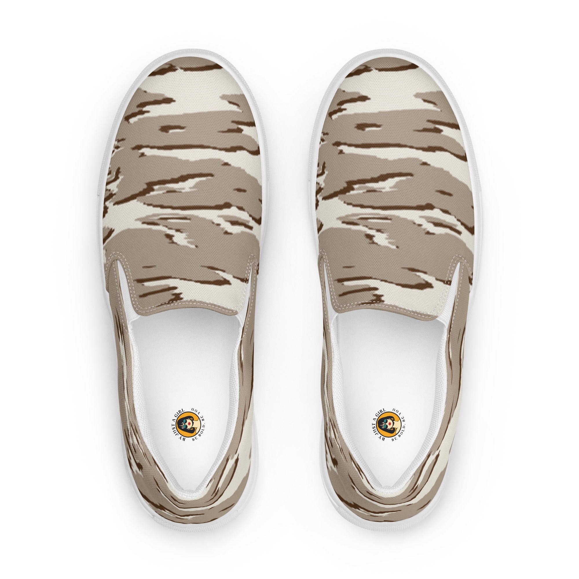 Ein Paar beiger Slip-On Canvas Schuhe mit einem wellenförmigen Camouflage-Muster in Hellbeige und Dunkelbeige. Die Sohle ist weiß. Die Schuhe sind leicht nach links gedreht, sodass die Vorderseite beider Schuhe sichtbar ist.