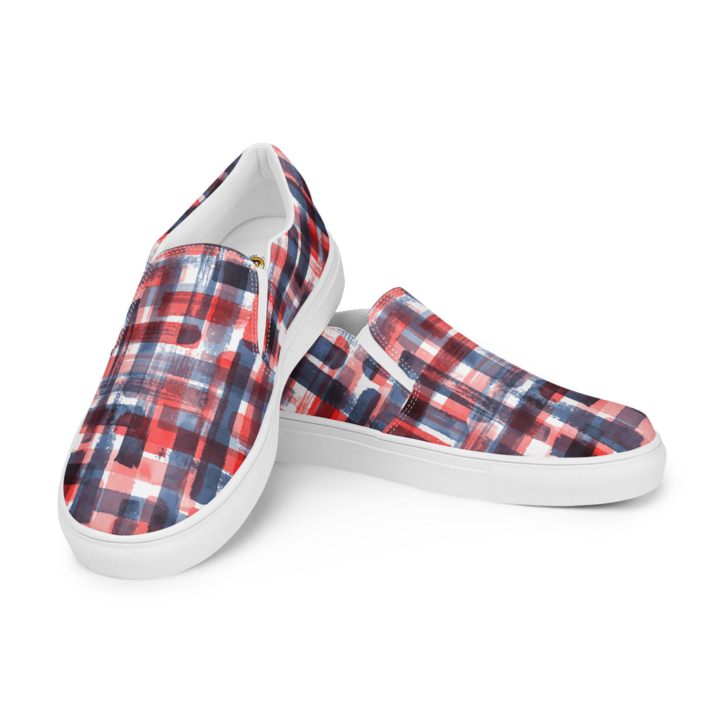 Ein Paar weißer Slip-On Canvas Schuhe mit einem abstrakten, gitterartigen Muster aus breiten, transparenten Pinselstrichen in Rot, Dunkelblau und Hellblau, die sich überlappen und ein kariertes Aussehen erzeugen. Die Sohle ist weiß. Die Schuhe sind leicht nach links gedreht, sodass die Vorderseite beider Schuhe sichtbar ist.