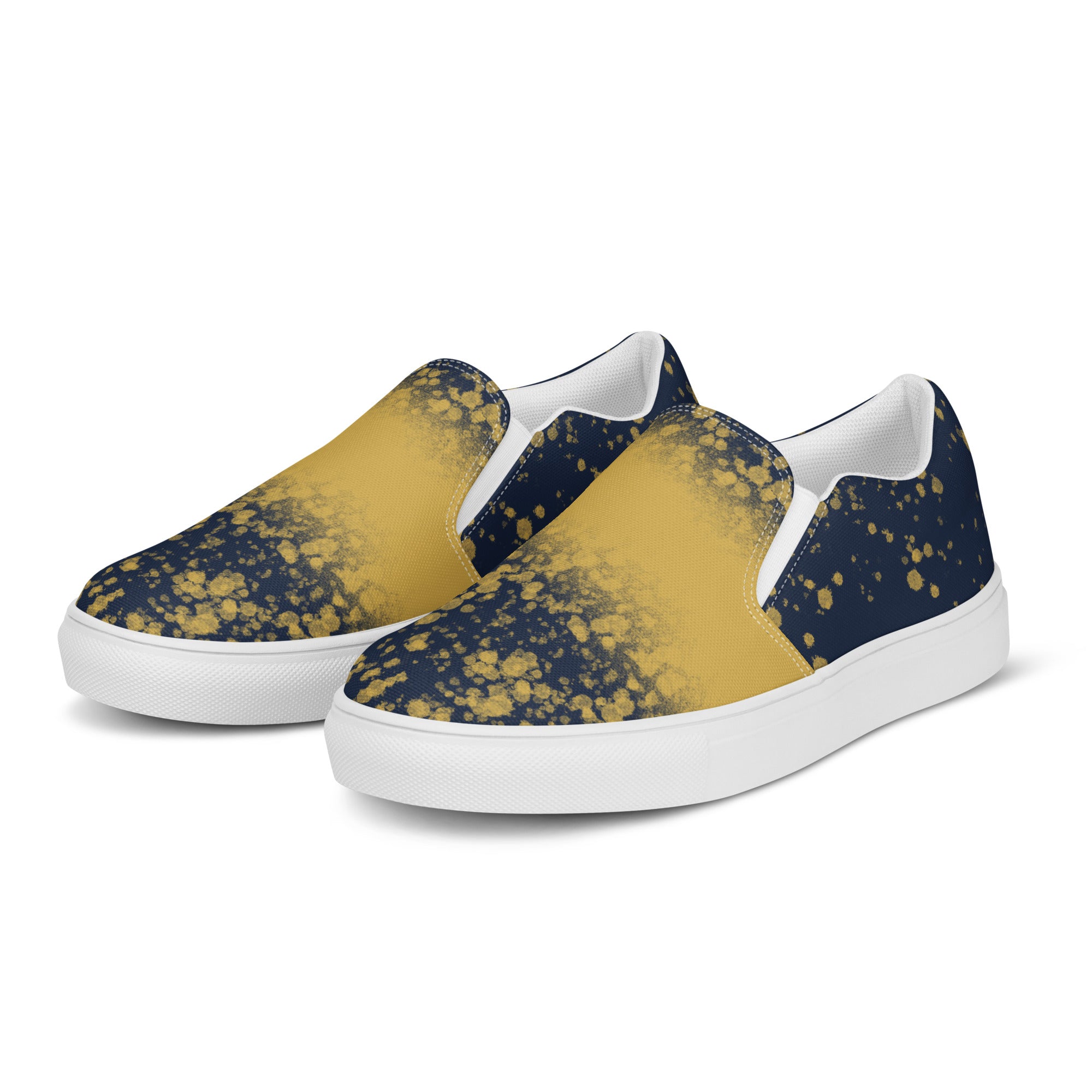 Ein Paar dunkelblauer Slip-On Canvas Schuhe mit einem Muster aus goldenen Farbspritzern, die von der Mitte des Schuhs nach außen hin weniger werden. Die Sohle ist weiß. Die Schuhe sind leicht nach links gedreht, sodass die Vorderseite beider Schuhe sichtbar ist.