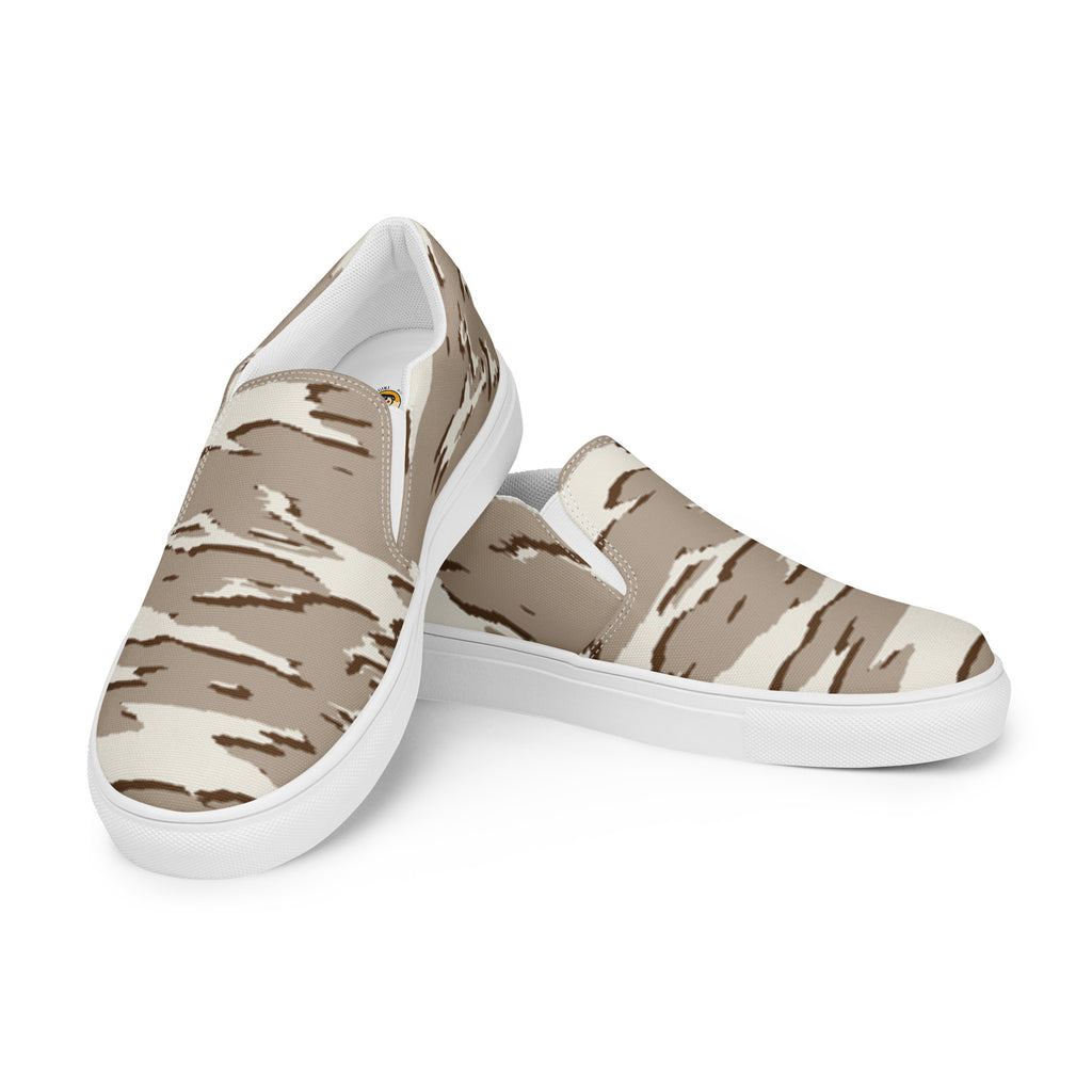 Ein Paar beiger Slip-On Canvas Schuhe mit einem wellenförmigen Camouflage-Muster in Hellbeige und Dunkelbeige. Die Sohle ist weiß. Die Schuhe sind leicht nach links gedreht, sodass die Vorderseite beider Schuhe sichtbar ist.