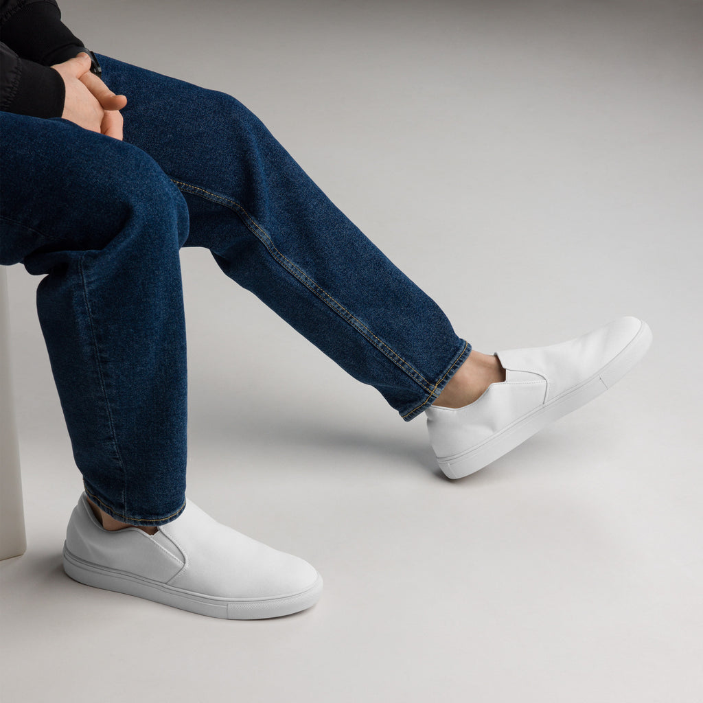 Ein Paar reinweißer Slip-On Canvas Schuhe, die auf einem weißen Hintergrund stehen. Die Schuhe sind schlicht und ohne Muster. Die Sohle ist ebenfalls weiß. Die Schuhe sind leicht nach links gedreht, sodass die Vorderseite beider Schuhe sichtbar ist.