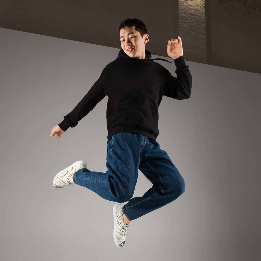 Ein Paar cremefarbener Slip-On Canvas Schuhe mit einem Muster aus schwarzen Punkten. Die Punkte sind am Rand des Schuhs größer und werden zur Mitte hin kleiner. Die Sohle ist weiß. Die Schuhe sind leicht nach links gedreht, sodass die Vorderseite beider Schuhe sichtbar ist.