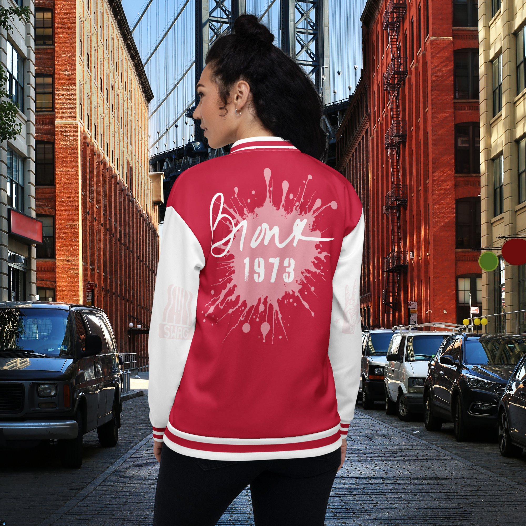 Das Model trägt eine rot-weiße Jacke. Auf der Rückenansicht ist ein großer altrosa farbener klecks  darauf steht mit weißer Schreibschrift Bronx und darunter in alter Industrieschrift 1973. Auf dem linkel Ärmel ist das Swag zeichen zu sehen sowie auf dem rechten ärmel das Peace Fingerzeichen mit Blitzen drumherum. Beide Elemente wurden in einem altrosea sehr dezent dargestellt. By Just a Girl.